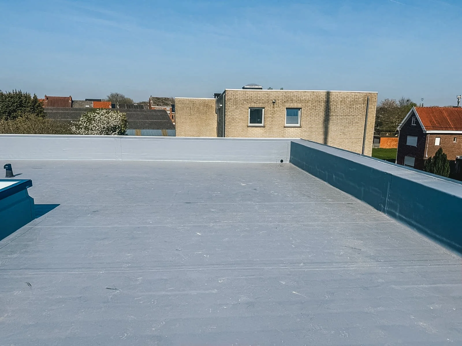 Uitzicht vanaf een plat dak met een blauwe lucht en enkele huizen op de achtergrond.