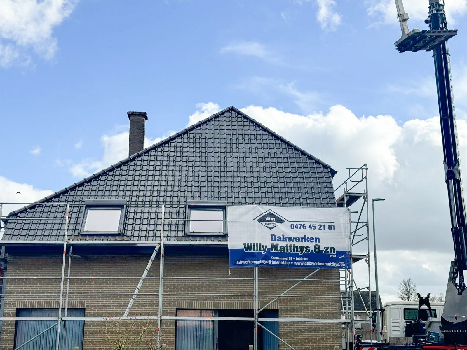 Een huis dat wordt gerenoveerd met steigers rondom. Er hangt een bord met de naam 'Willy Mathys & zn' en contactgegevens.