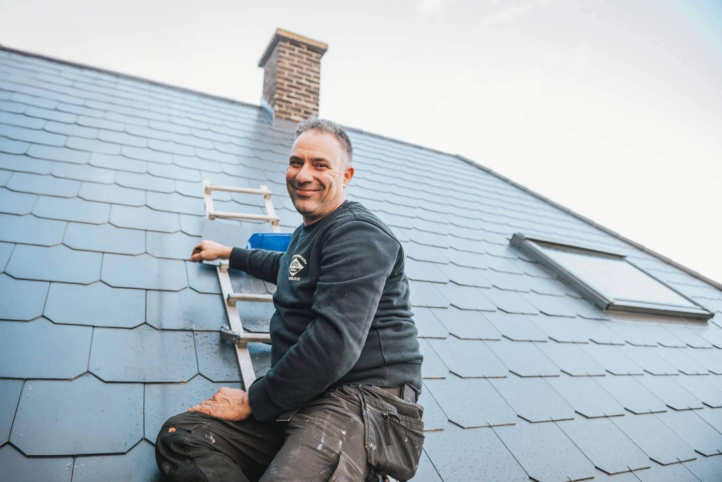Man die dakbedekkingswerkzaamheden uitvoert op een schuine dak met grijze dakpannen.