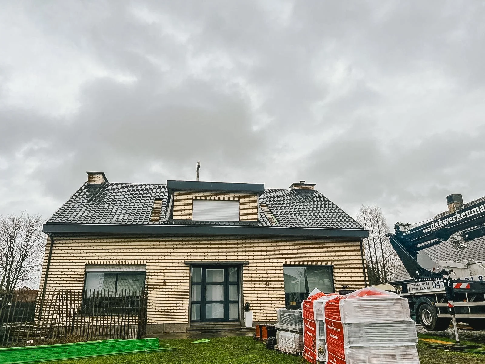 Nieuwbouw woning met dakwerkzaamheden, bouwmaterialen en een hoogwerker op de oprit.