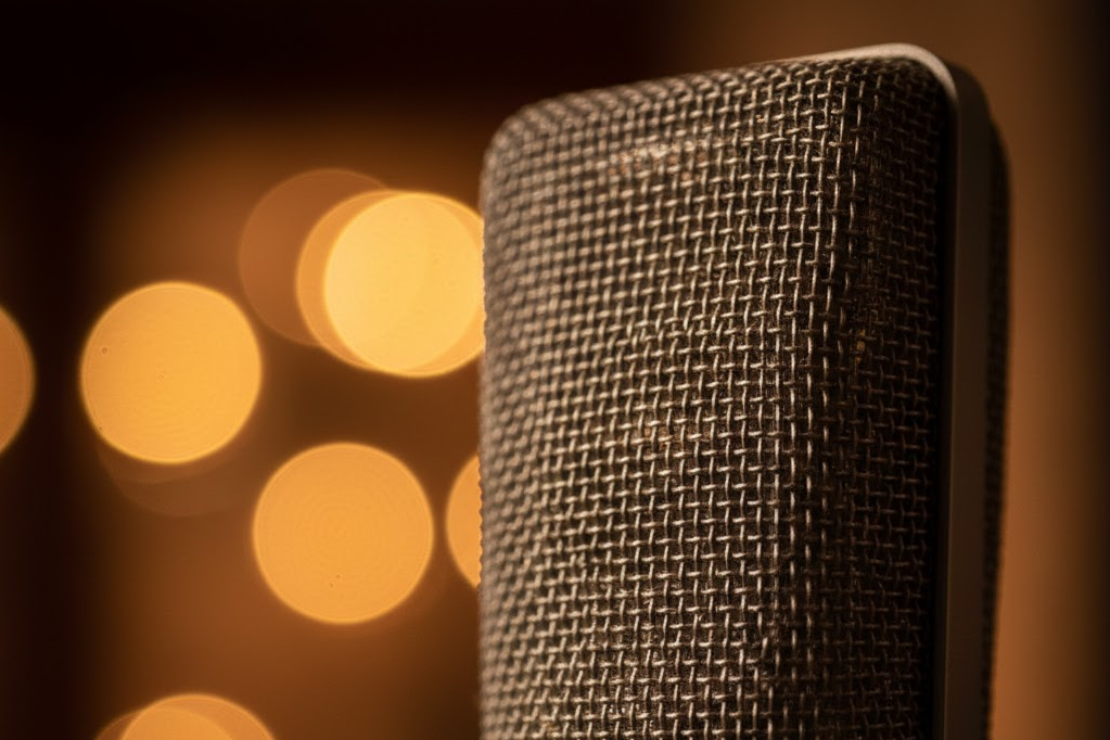 Nahaufnahme eines Mikrofons vor einer warm beleuchteten, unscharfen Hintergrundbeleuchtung.