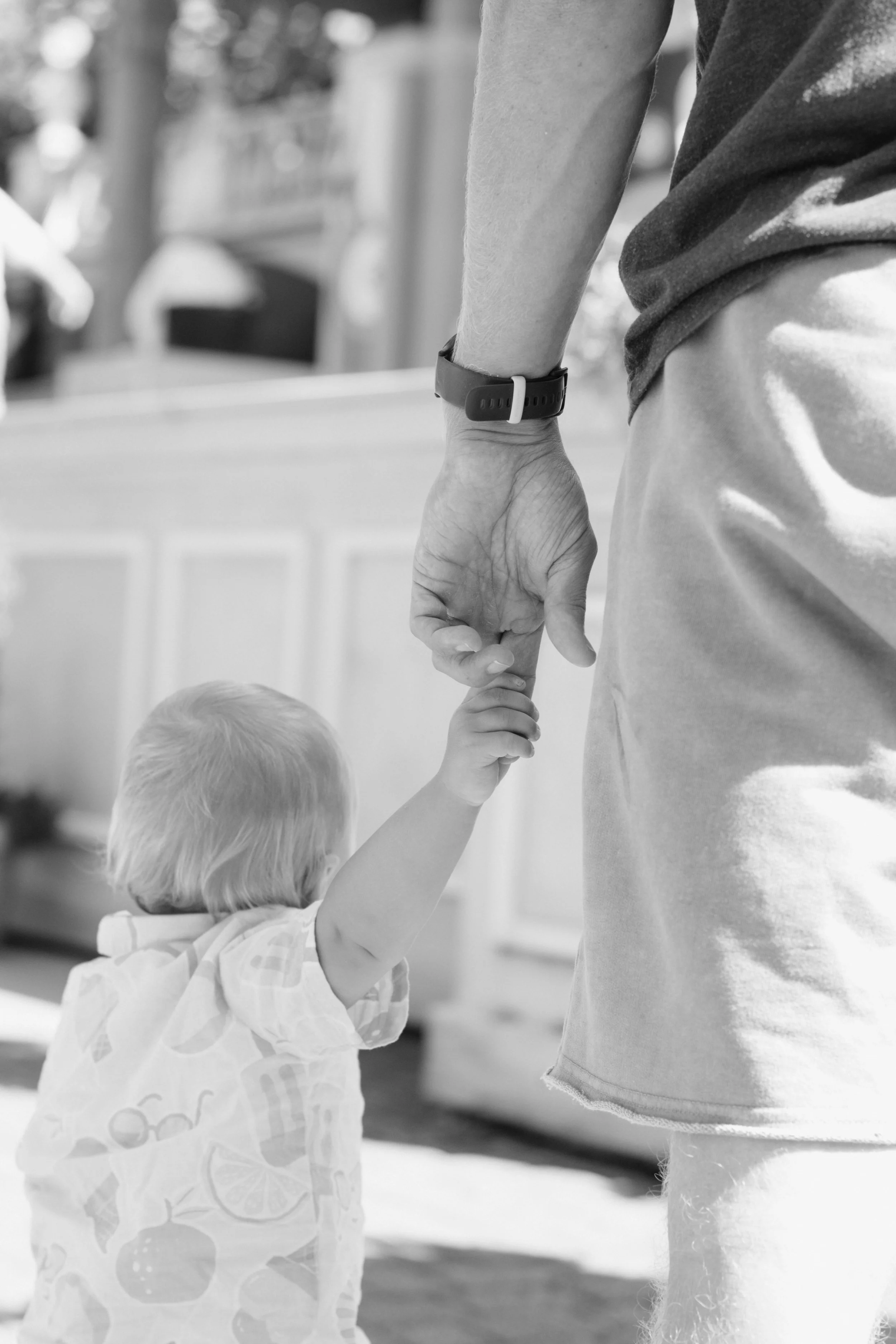 Ein Kleinkind hält die Hand des Vaters, beim Gehen im Freien, in schwarz-weiß.