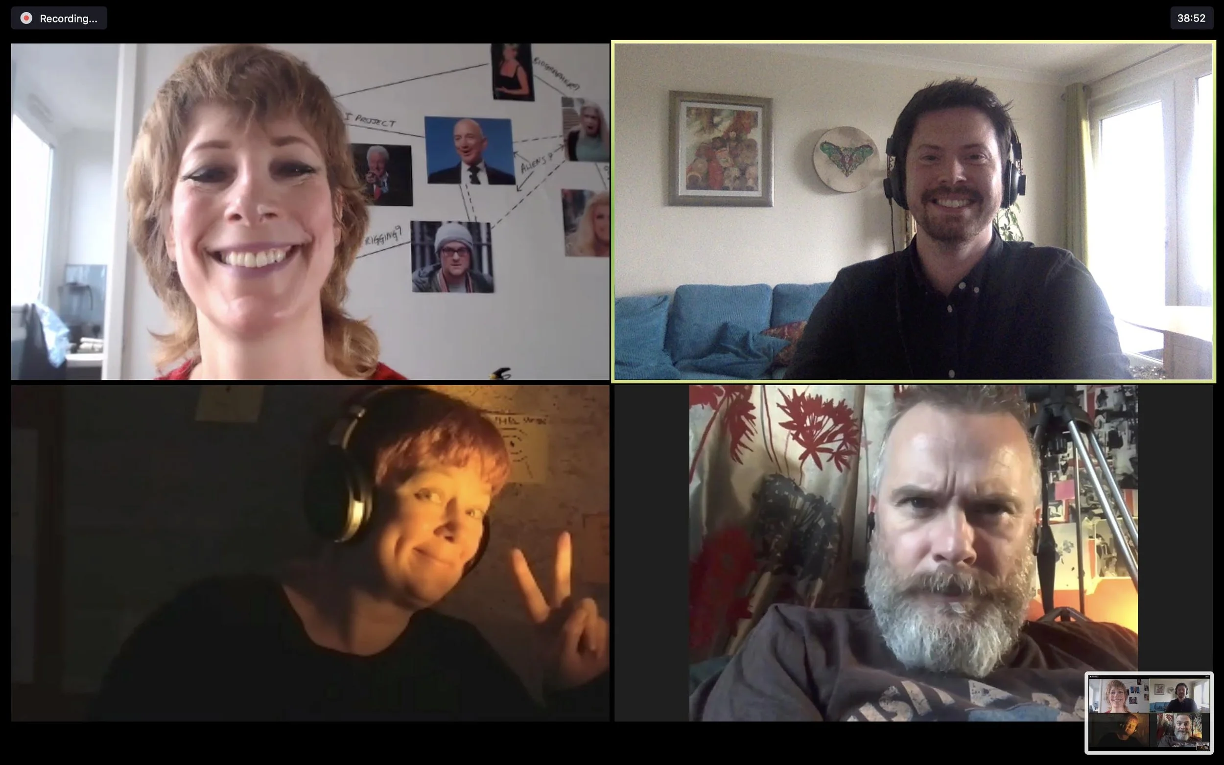 Four people participating in a video call, each in their own environment. The woman in the top left has short curly hair and is smiling; behind her is a wall with photos and notes. The man in the top right has dark hair and a beard, wearing headphones, sitting on a blue couch in a room with framed artwork. n the bottom left has short hair, wearing large headphones, making a peace sign with his hand in a dimly lit room. The older man in the bottom right has a gray beard, wearing a headset, in front of a red and white patterned curtain with various items in the background.
