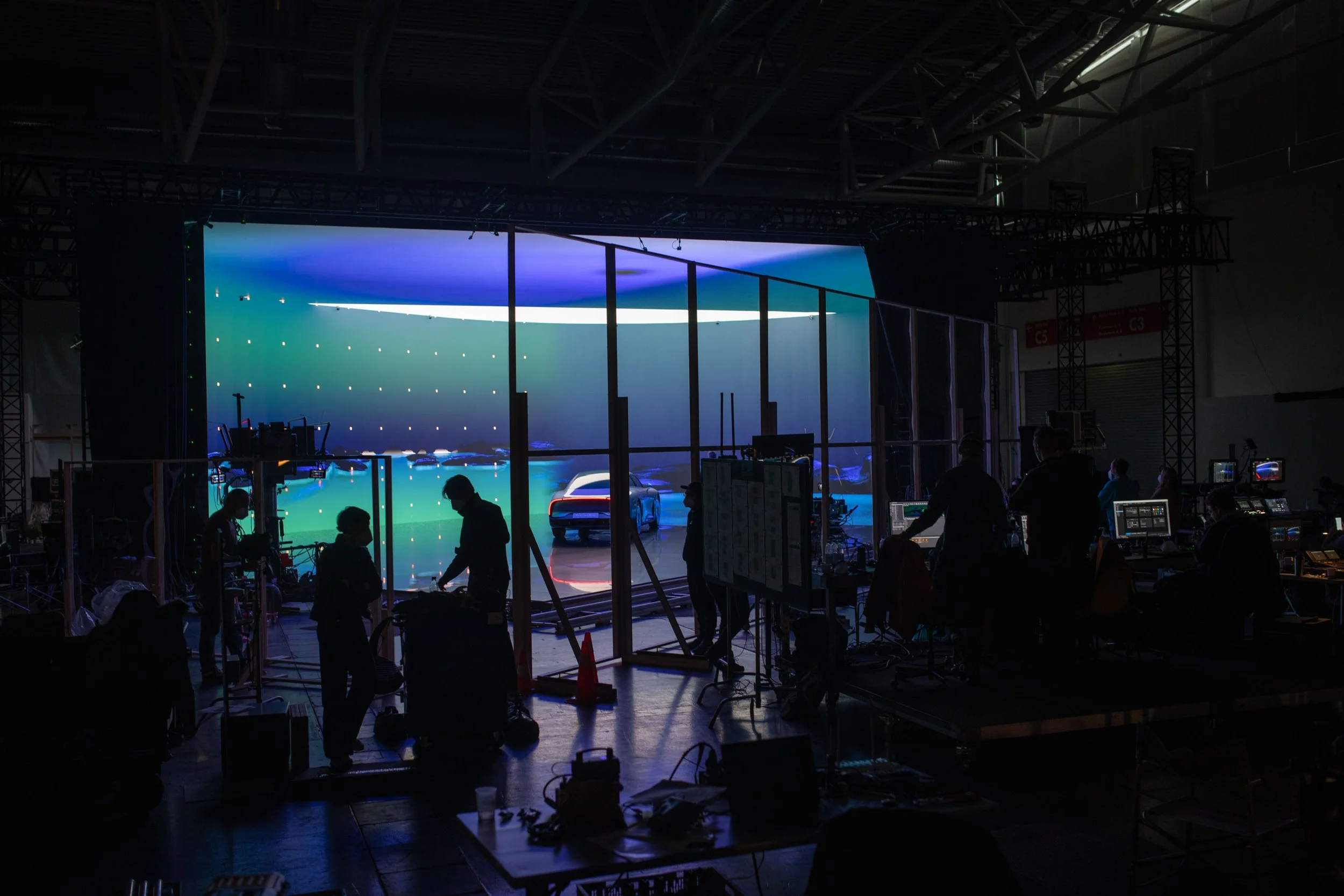 Menschen arbeiten an einem großen, dunklen Veranstaltungs- oder Filmset mit digitaler Hintergrundprojektion, in einem großen Raum mit hoher Decke.