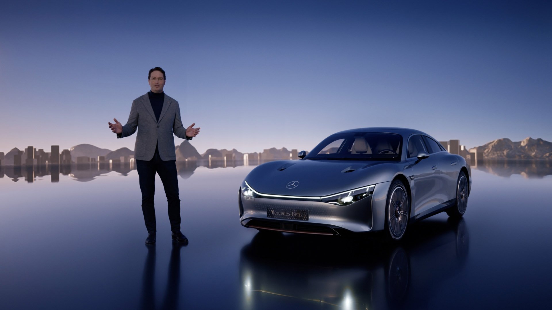 Ein Mann in schwarzem Hemd und grauem Blazer steht vor einem schwarzen Mercedes-Benz Auto im futuristischen Stadtbild mit Wasserfläche im Hintergrund.