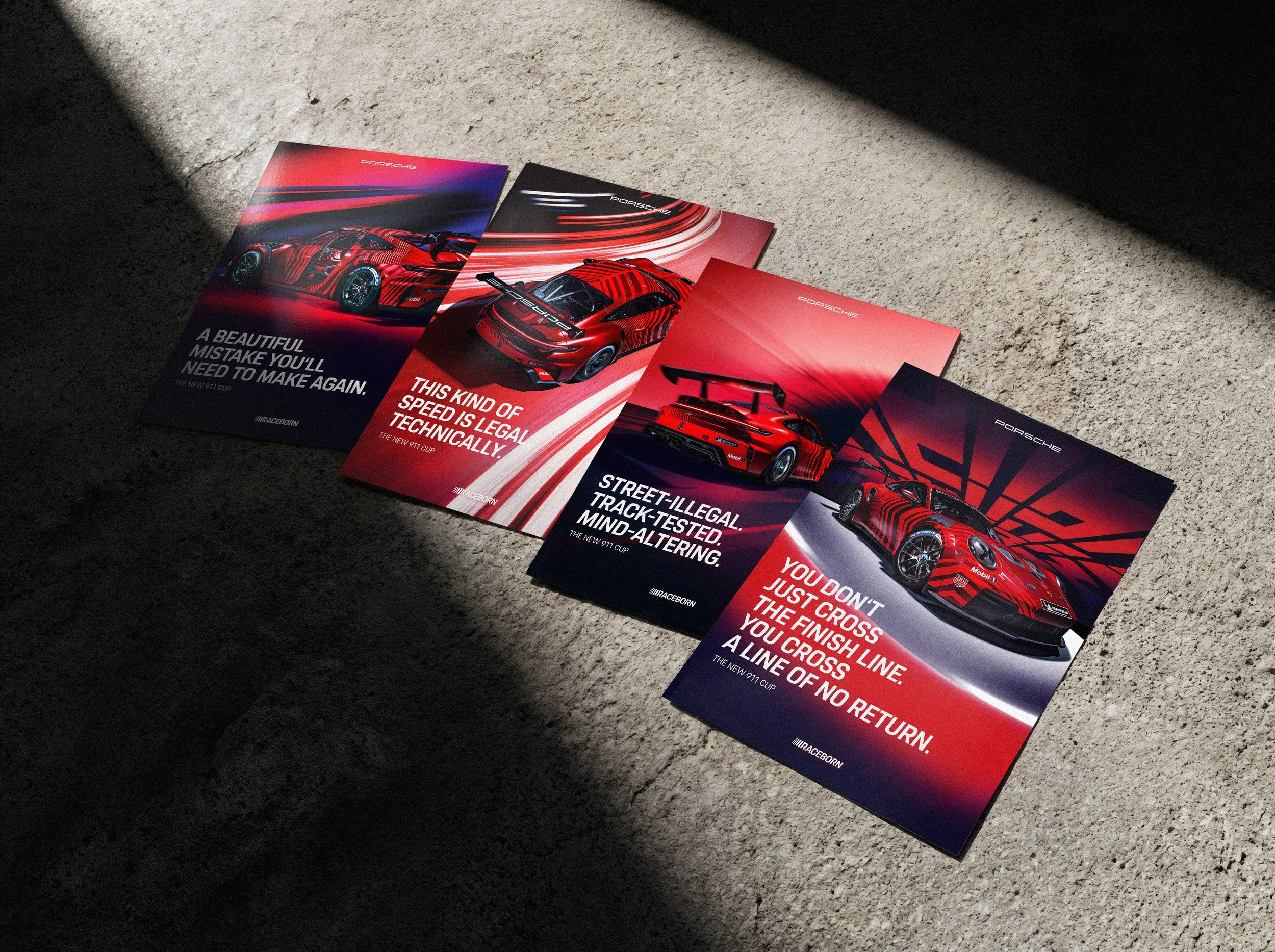 Drei Porsche-Broschüren auf einem rauen Gehweg, beleuchtet von Sonnenlicht, zeigen rote Sportwagen und enthalten Texte zu Geschwindigkeit, technischer Legalität und Rennsport.