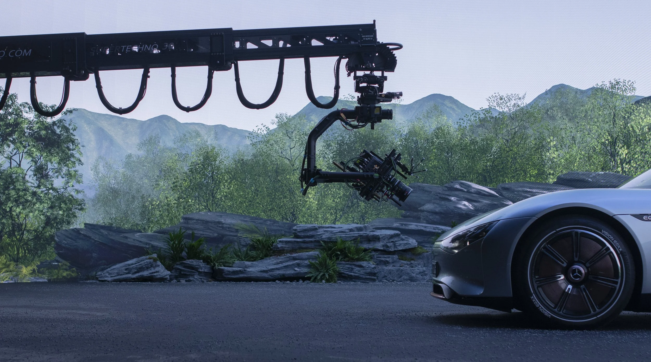 Ein Drohnen-Kamera-Setup vor einer Kamera eines Autos auf einer Landschaft mit Bergen und Büschen.