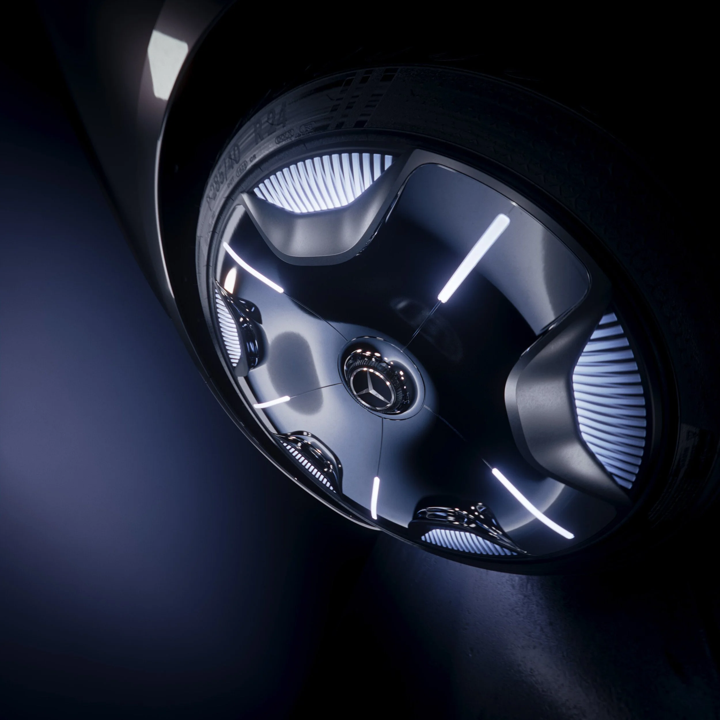 Nahaufnahme eines Mercedes-Benz Logos an einem silbernen Fahrzeug mit moderner Beleuchtung.