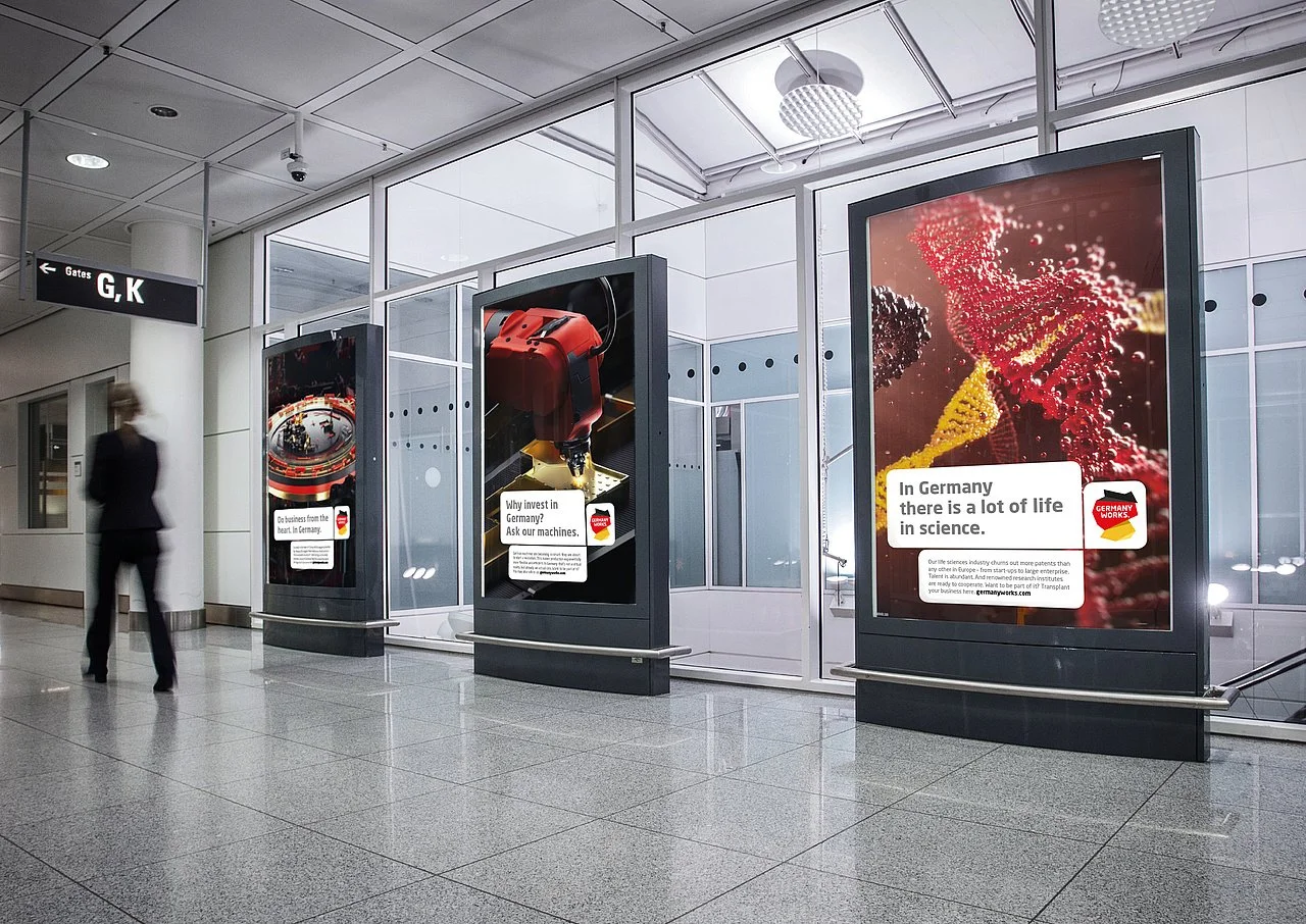 Werbetafeln in einem Flughafen mit Deutschland-Werbung, die wissenschaft und Innovation in Deutschland hervorhebt.