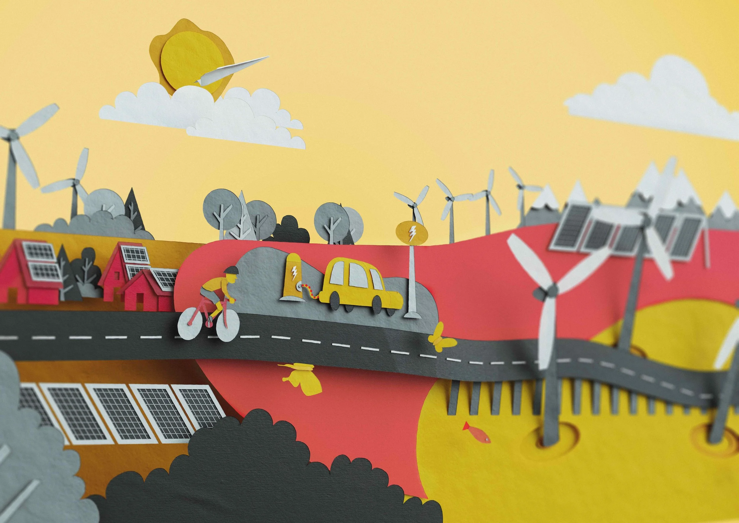 Papierkunstwerk zeigt eine ländliche Szene mit Windmühlen, Solarzellen, Häusern, Bäumen, einem Fahrradfahrer, einem Elektroauto und Windrädern, alles in bunten, vereinfachten Formen.