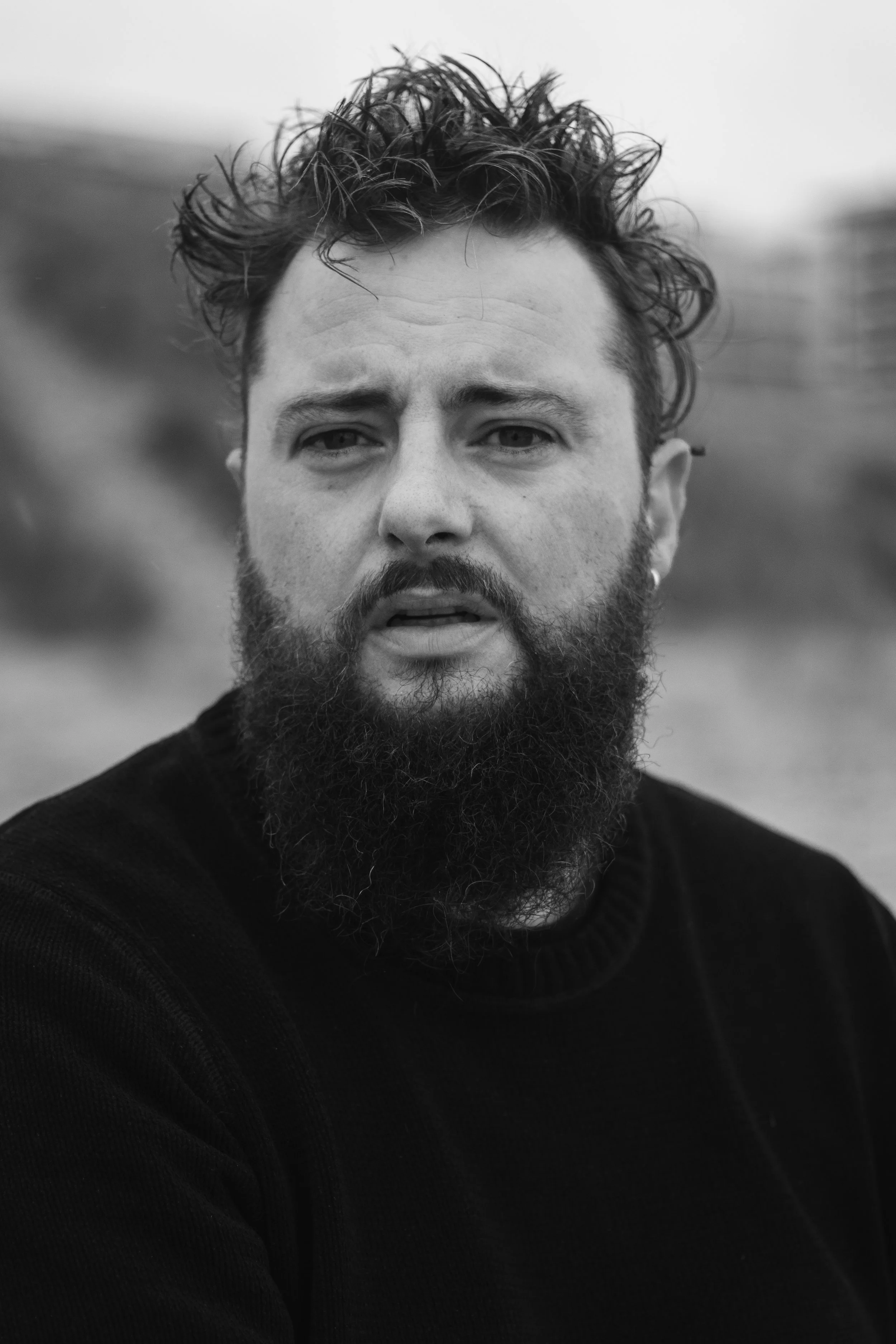 Zwarte en witte portretfoto van een man met een volle baard en warrig haar, die naar de camera kijkt.