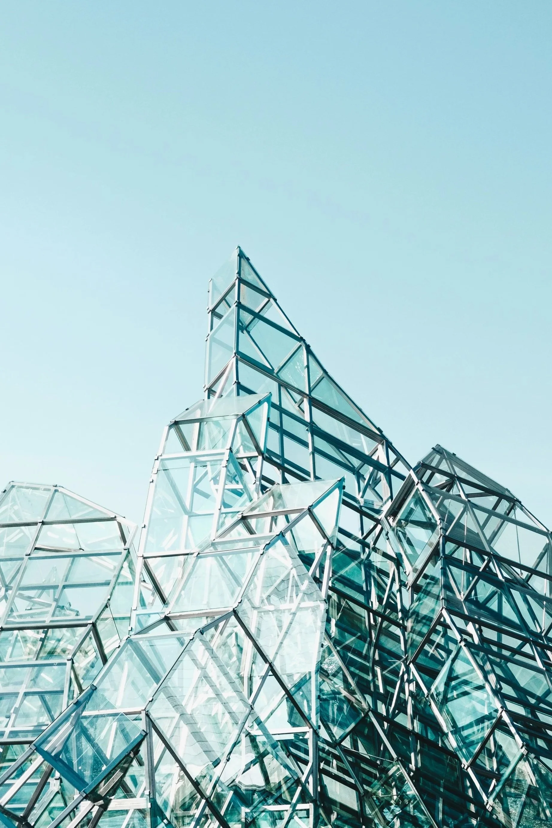Modern glass building with geometric design and clear blue sky background.