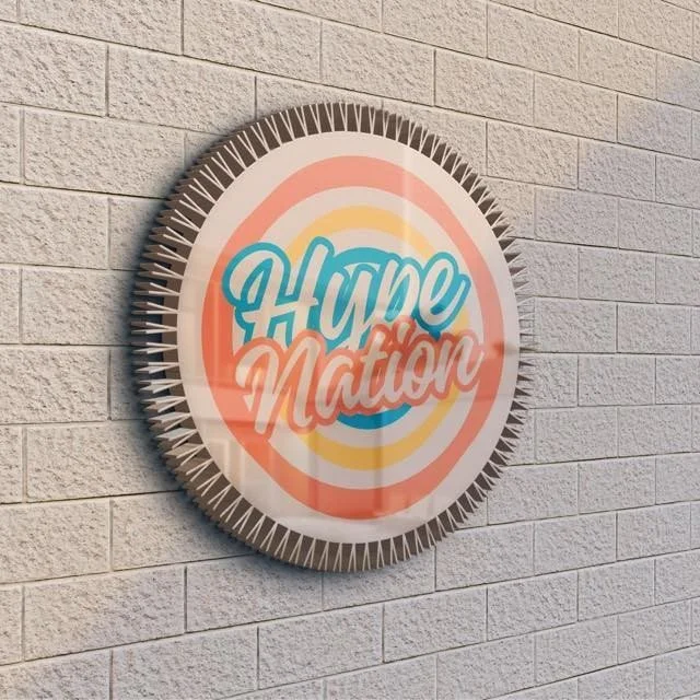 A circular wall decoration with the message "HYPE Nation" in colorful, stylized lettering, mounted on a textured light-colored brick wall.