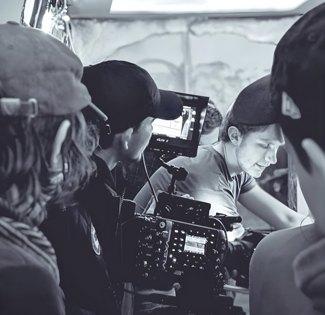 Filmmakers filming a scene with a camera and monitor, on a film set with crew members in the background.
