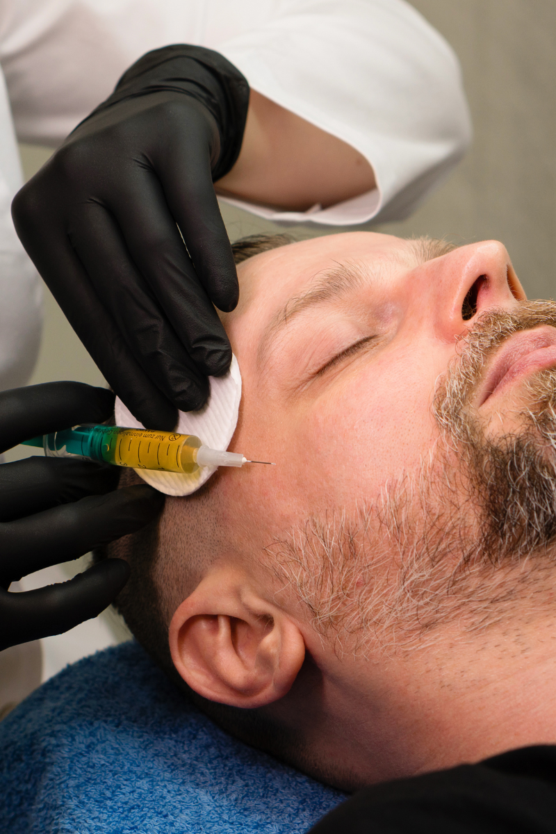 Ein Mann liegt auf einer Liege, während eine medizinische Fachkraft eine Injektion in die Wange setzt.