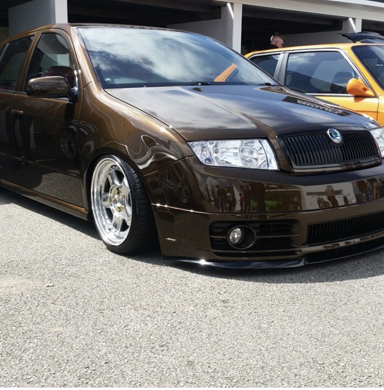 A brown Skoda car parked at an outdoor car show, with another yellow car in the background.