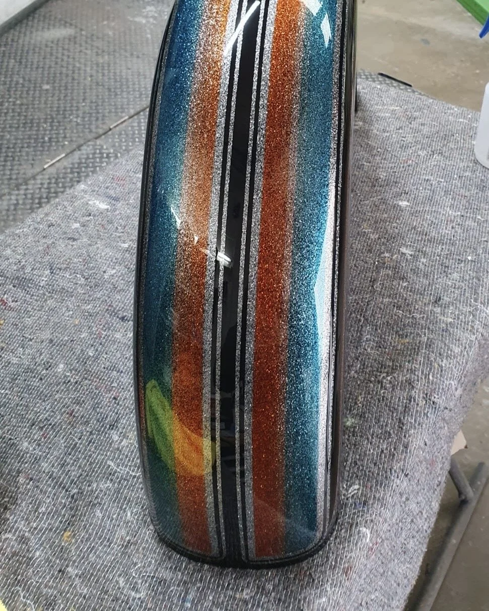 A motorcycle gas tank with a custom, glittery rainbow striped paint job.