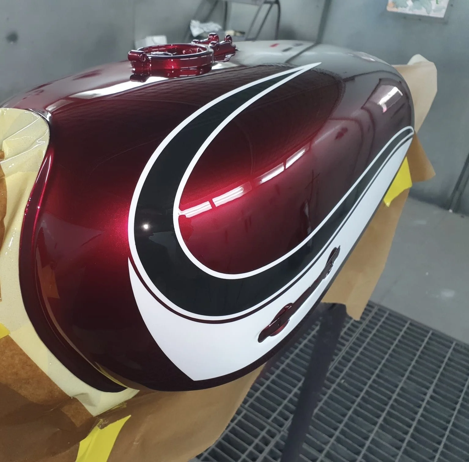 A close-up of a motorcycle fuel tank painted with a glossy black, maroon, and white design.
