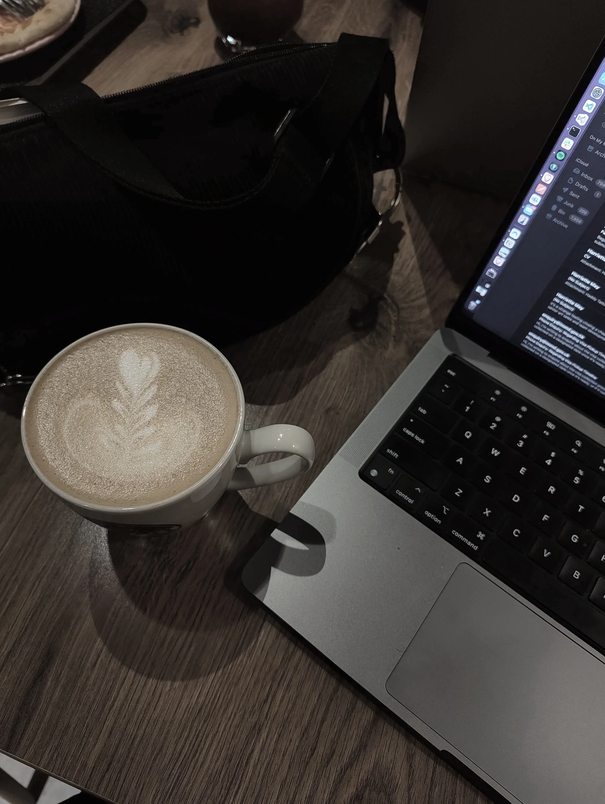 A laptop, a cup of latte with foam art, and a black bag on a wooden table. Doing admin and supporting business.