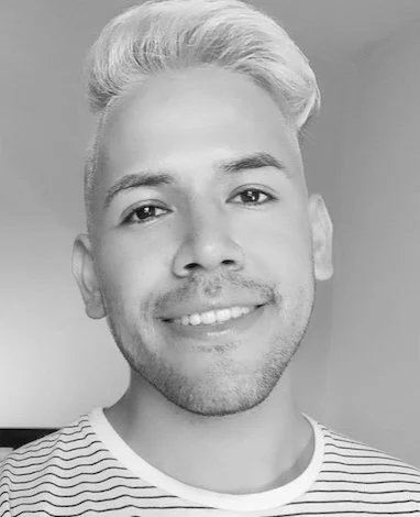 Black and white photo of a young man with light hair smiling, wearing a striped shirt.