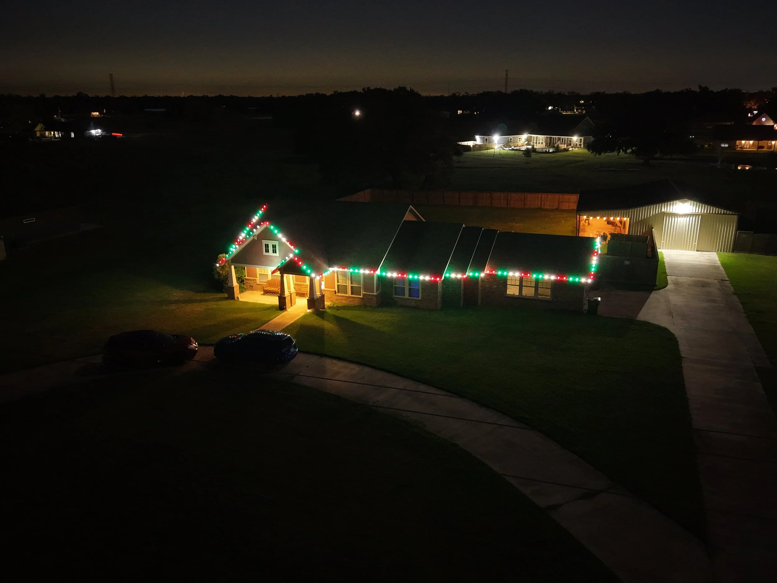 House decorated with Christmas lights at night, with a driveway and parked cars in the front