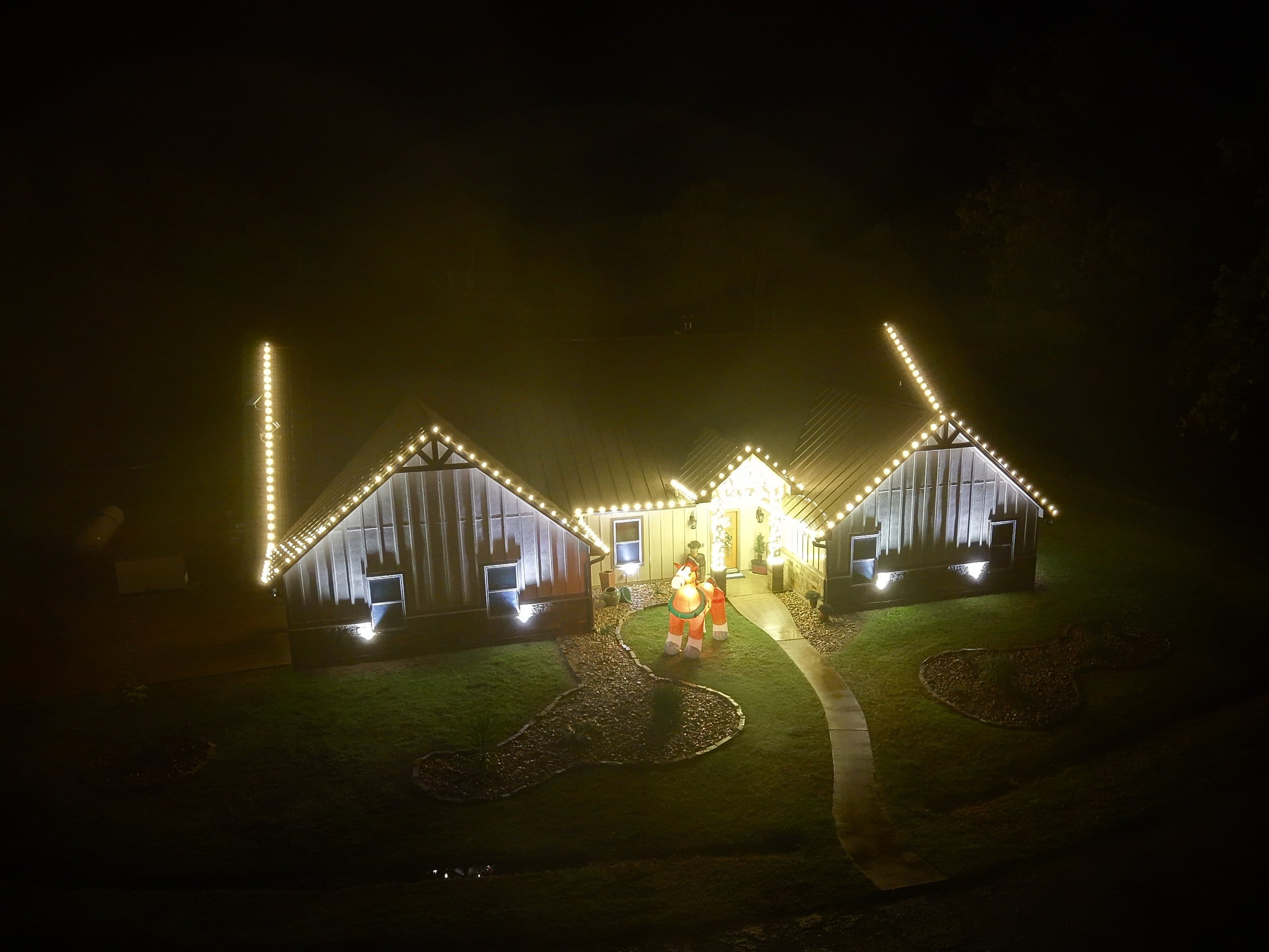 A house decorated with Christmas lights at night, featuring a Santa Claus figure, an inflatable reindeer, and illuminated pathways.