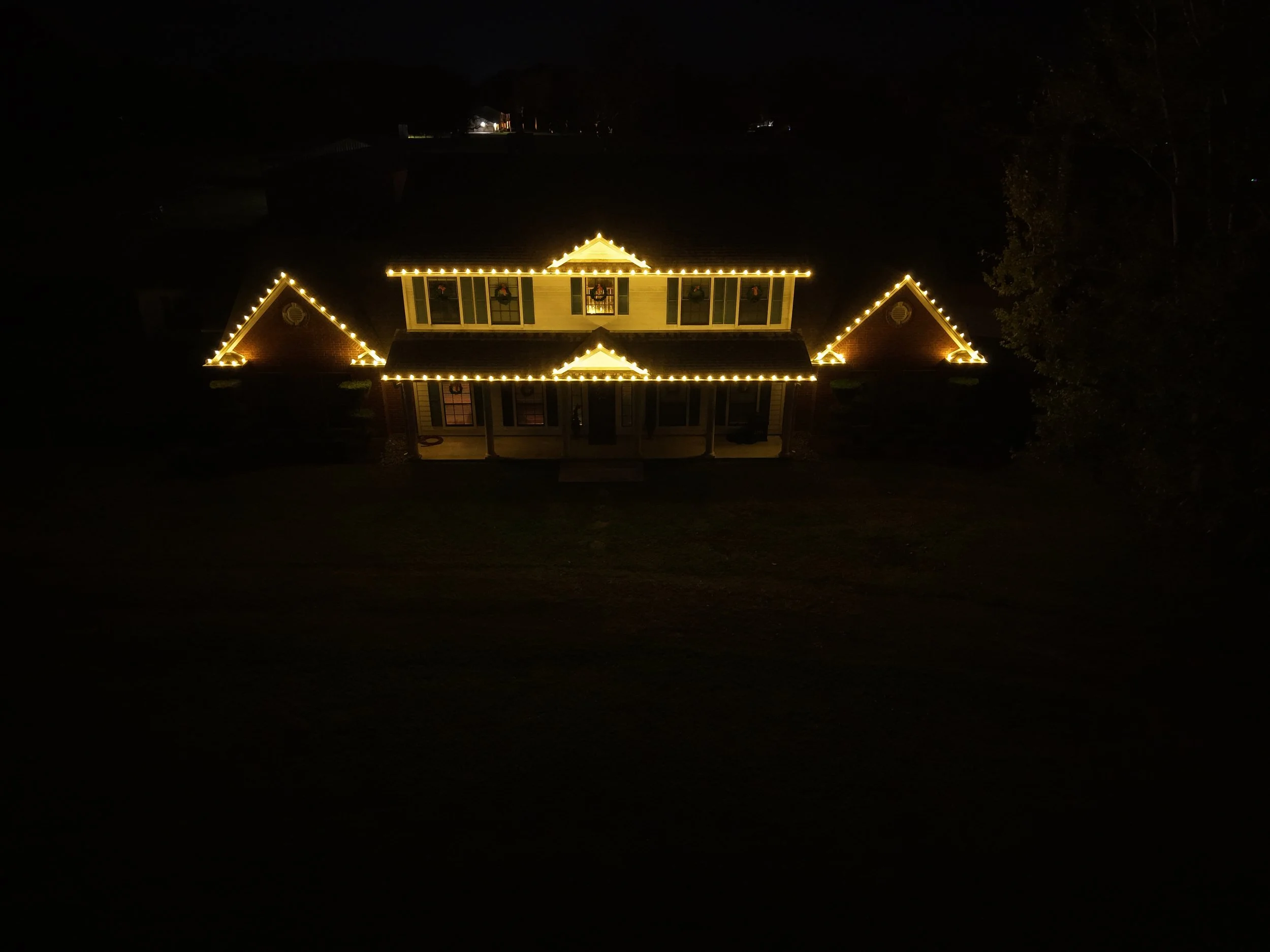 A house decorated with yellow string lights outlining the roof and windows, seen at night.
