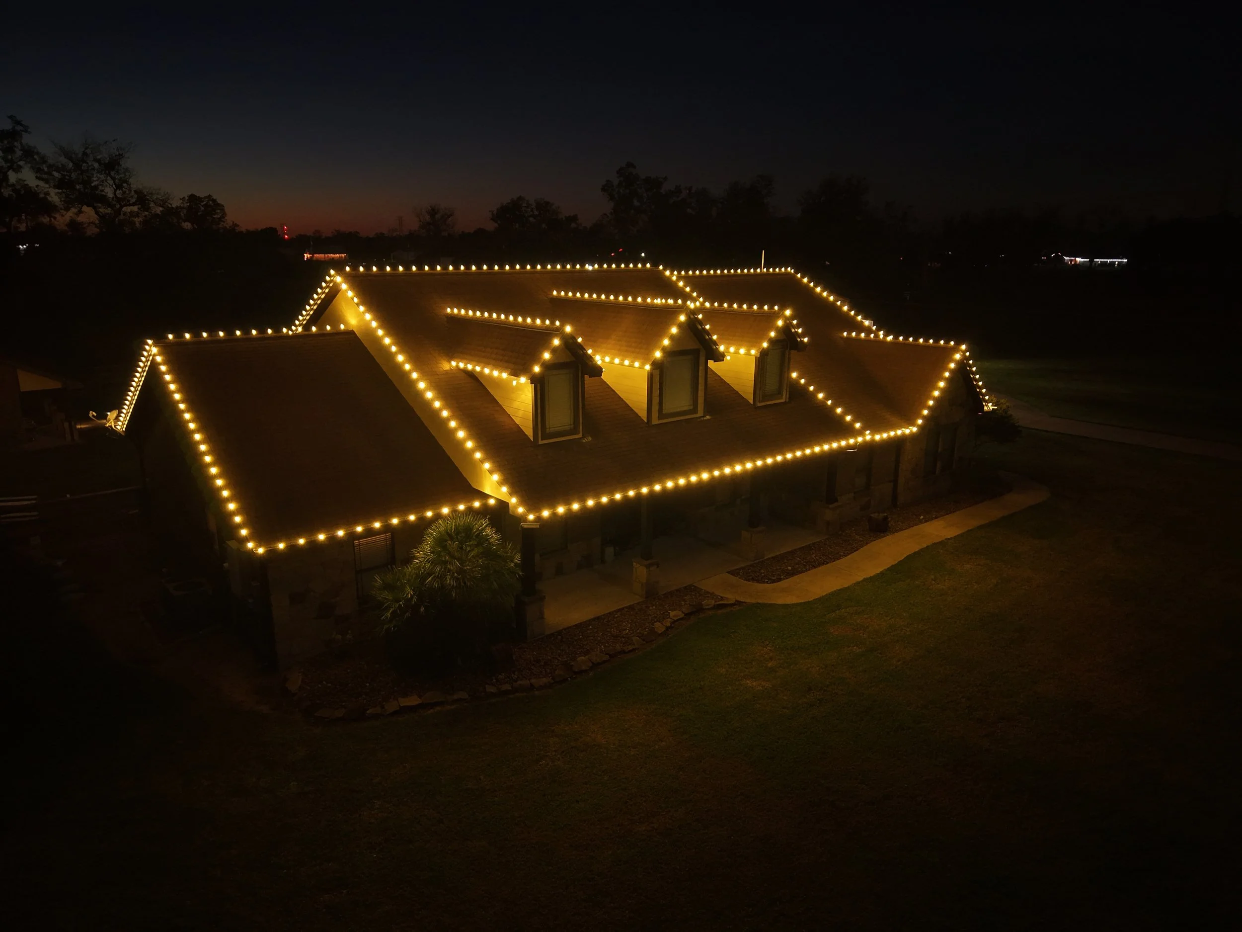 Nighttime view of a house decorated with yellow string lights outlining the roof and windows.