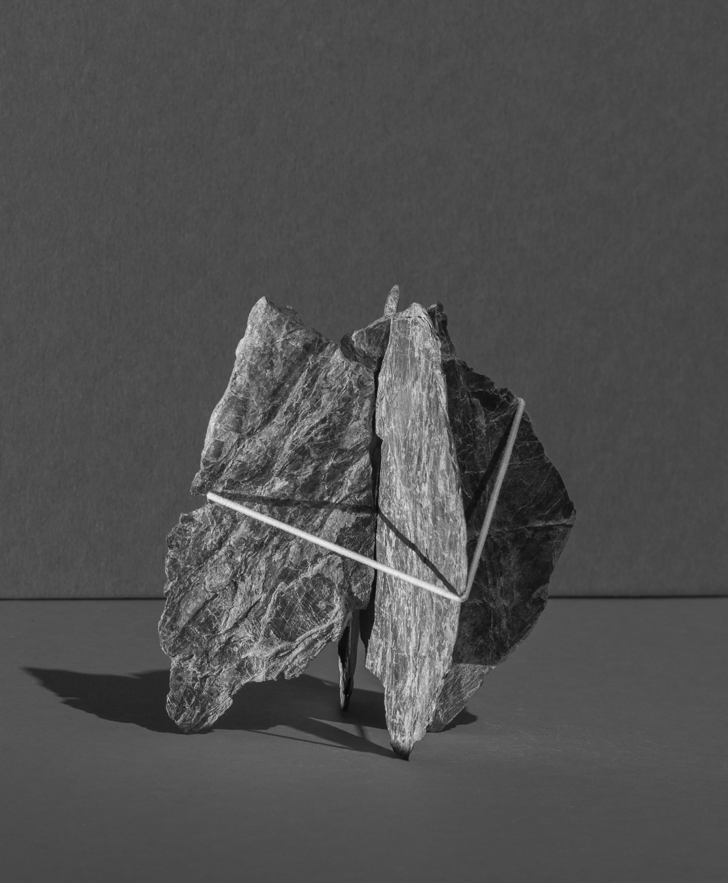Black and white photo of a rock sculpture held together with rubber bands, placed on a flat surface, against a plain background.