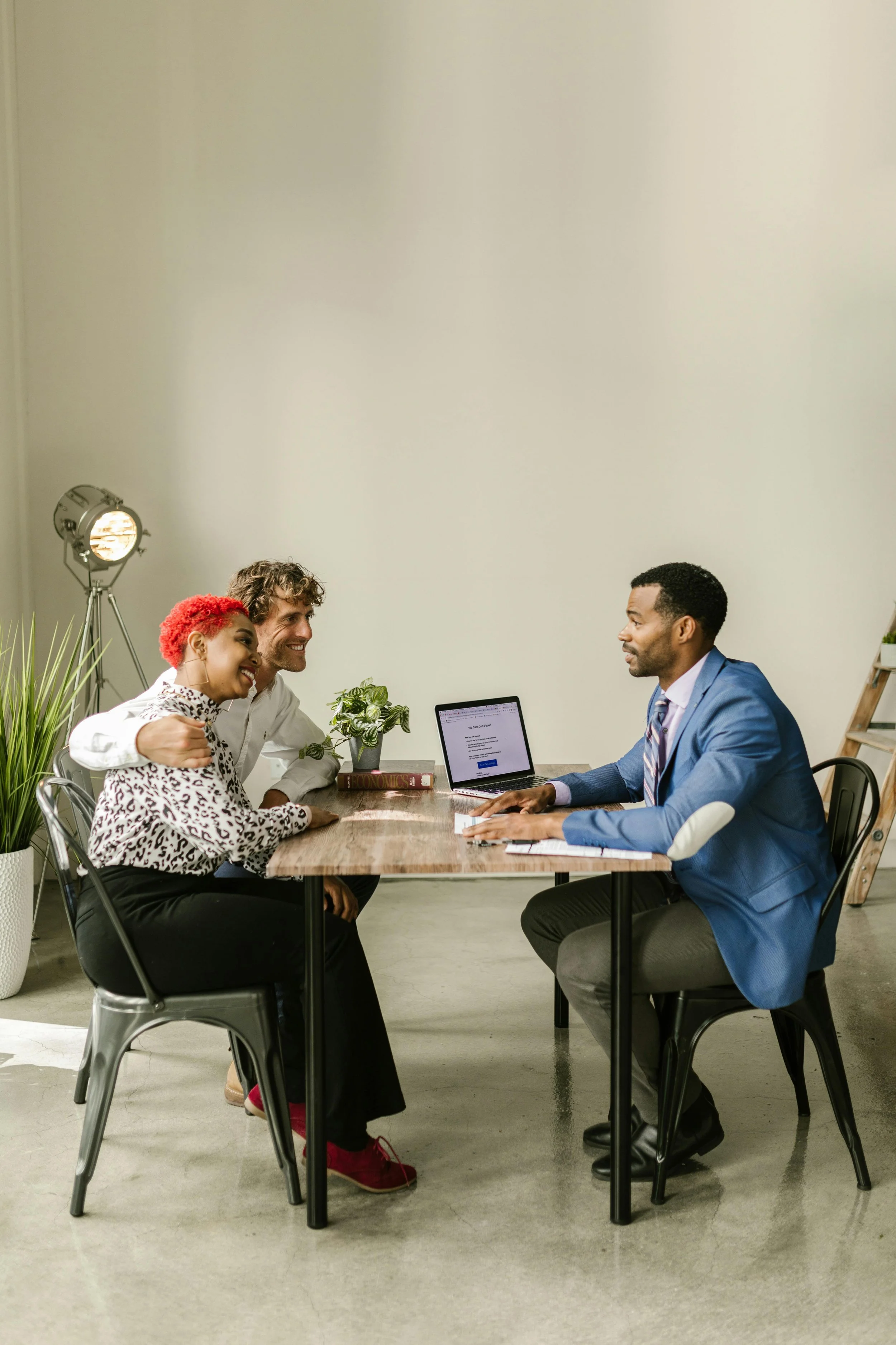 A couple sitting at a table with a man in a blue suit, a woman with red curly hair, and a man with brown curly hair, during a consultation in a modern office setting.