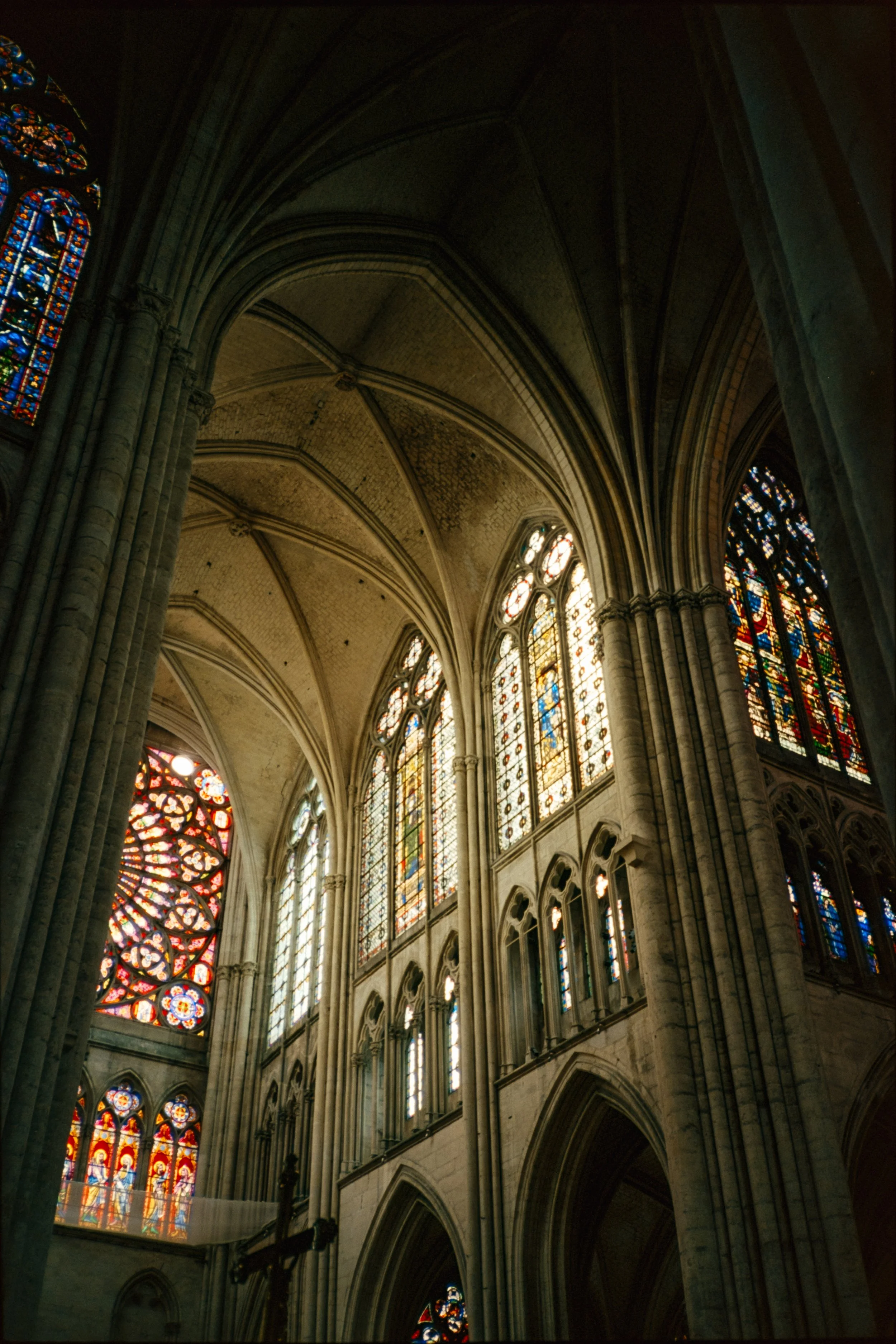 The interior of a Gothic cathedral with large stained glass windows and tall stone columns supporting ribbed arches.
