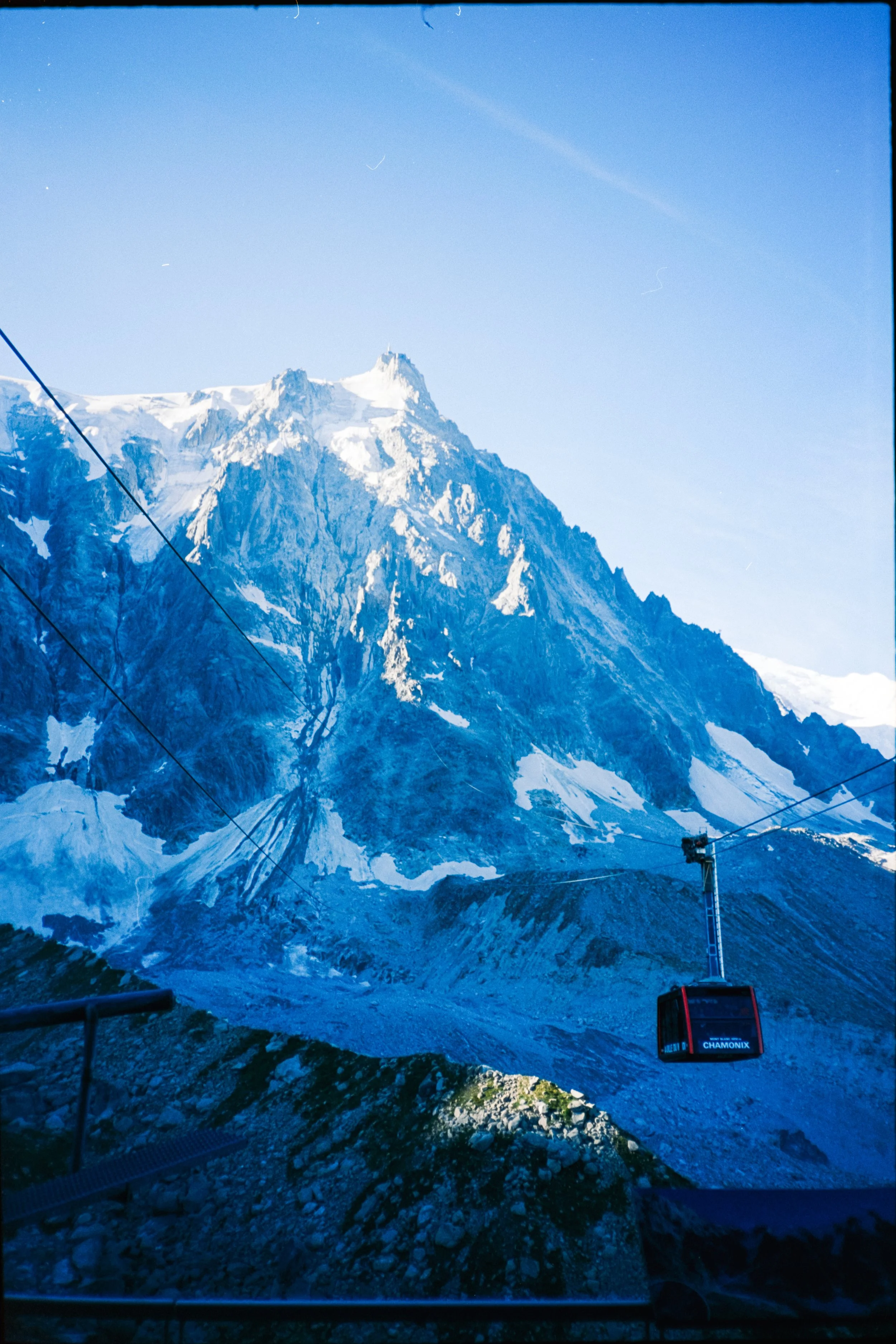 A mountain with snow-covered peaks under a clear blue sky, with cable cars in the foreground, one of which is labeled 'Chamonix'.