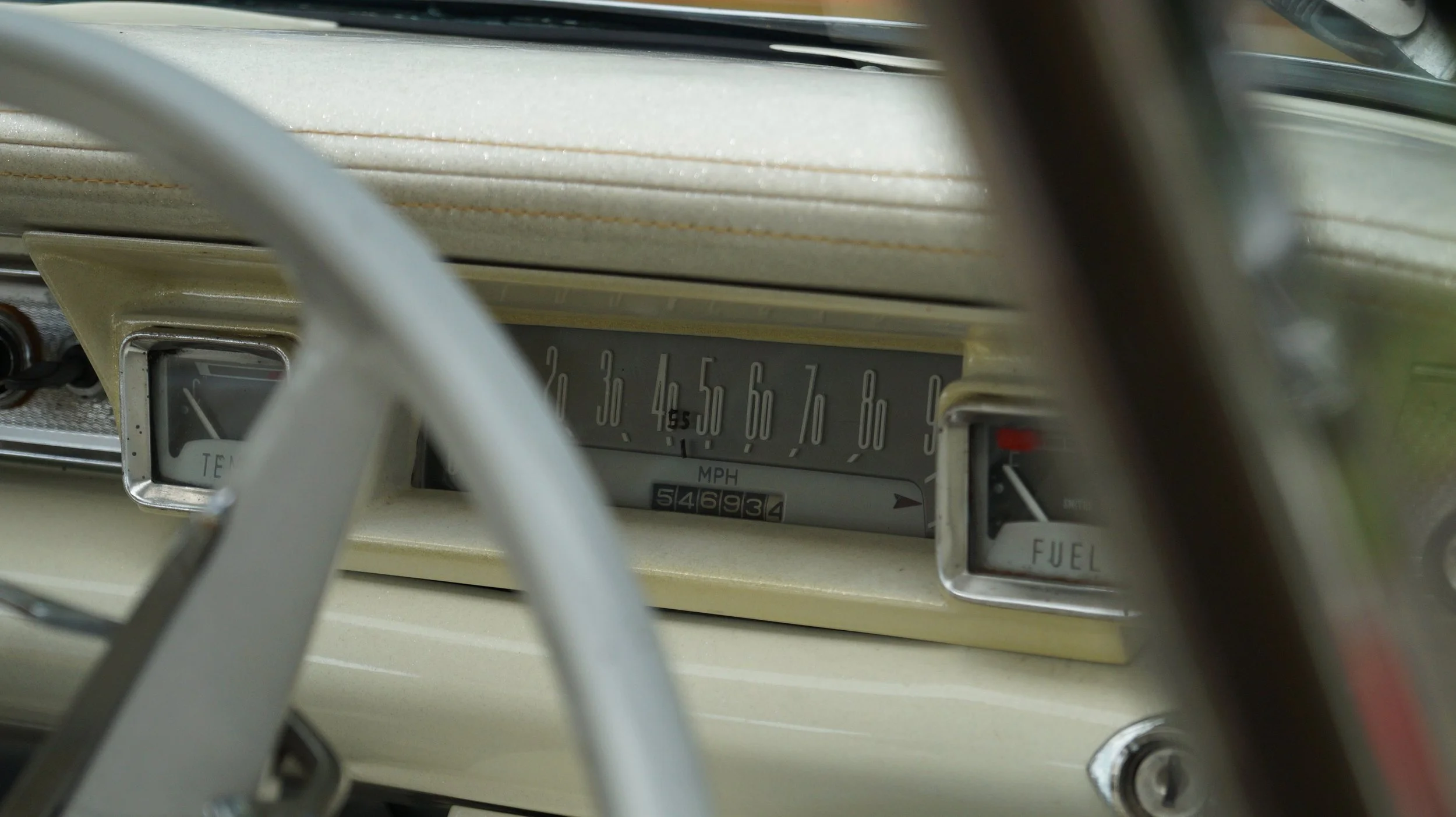 Close-up of a vintage car dashboard showing a speedometer, temperature, and fuel gauges.