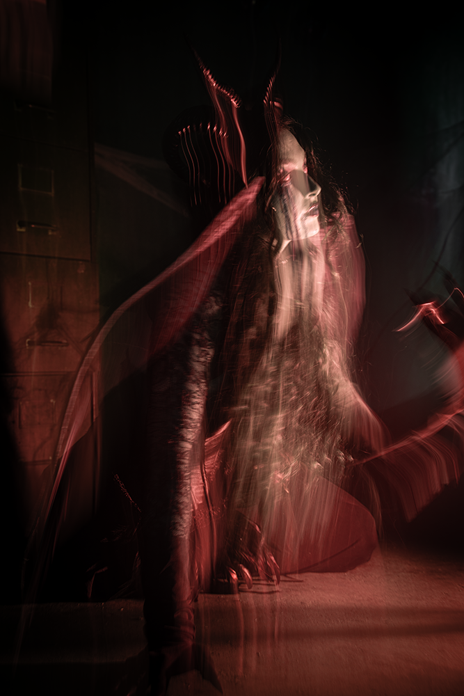 A blurred image of a woman with long hair and sunglasses, sitting with a dark background and red lighting effects.