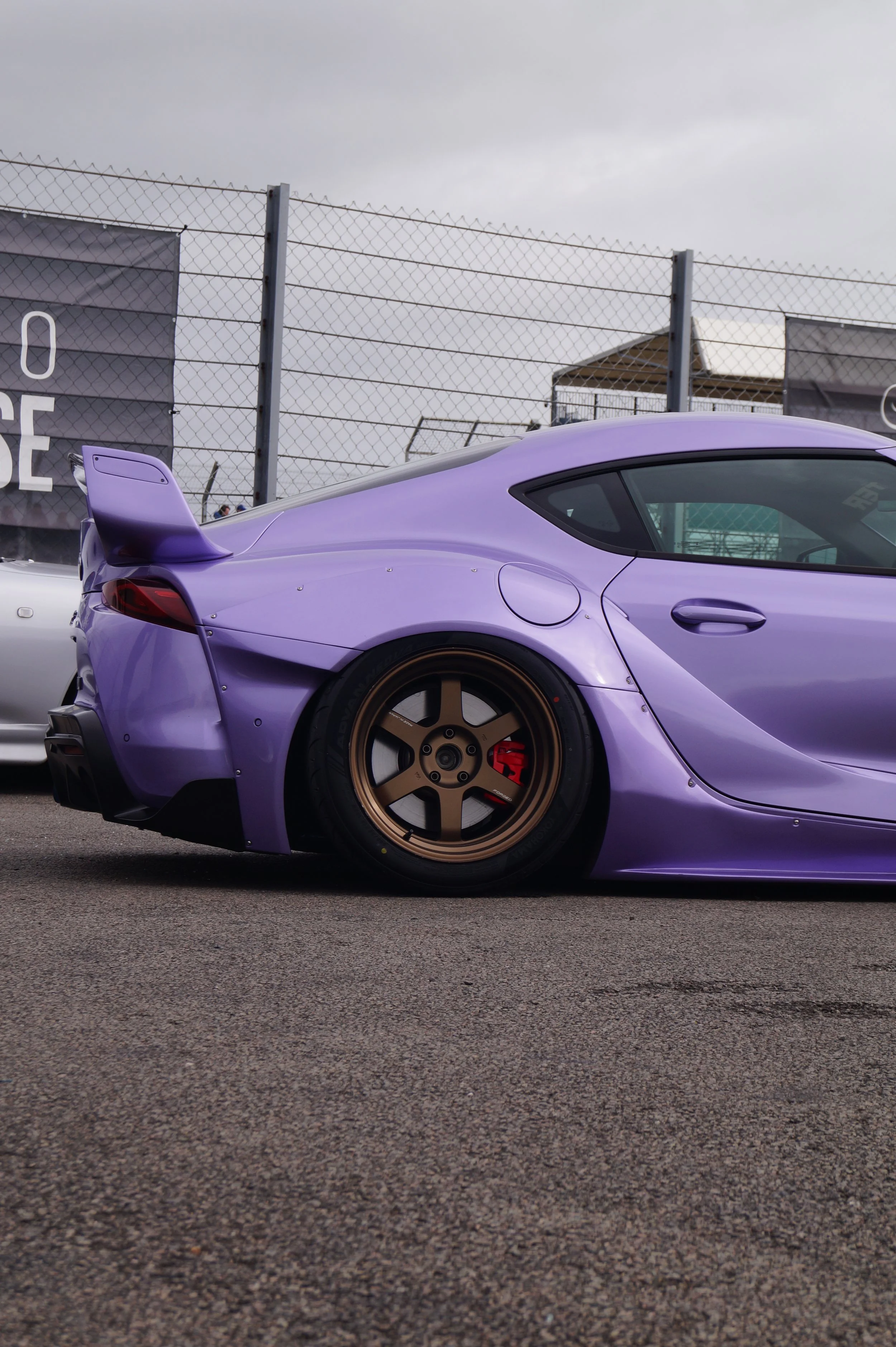 A purple sports car parked on a racetrack with gold wheels and a rear spoiler and aerodynamic body.