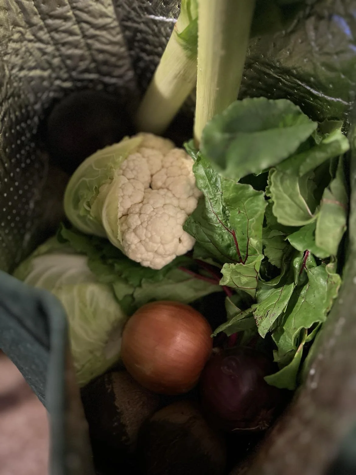 Fresh cauliflower, leafy greens, an onion, and a purple onion inside a reusable shopping bag.