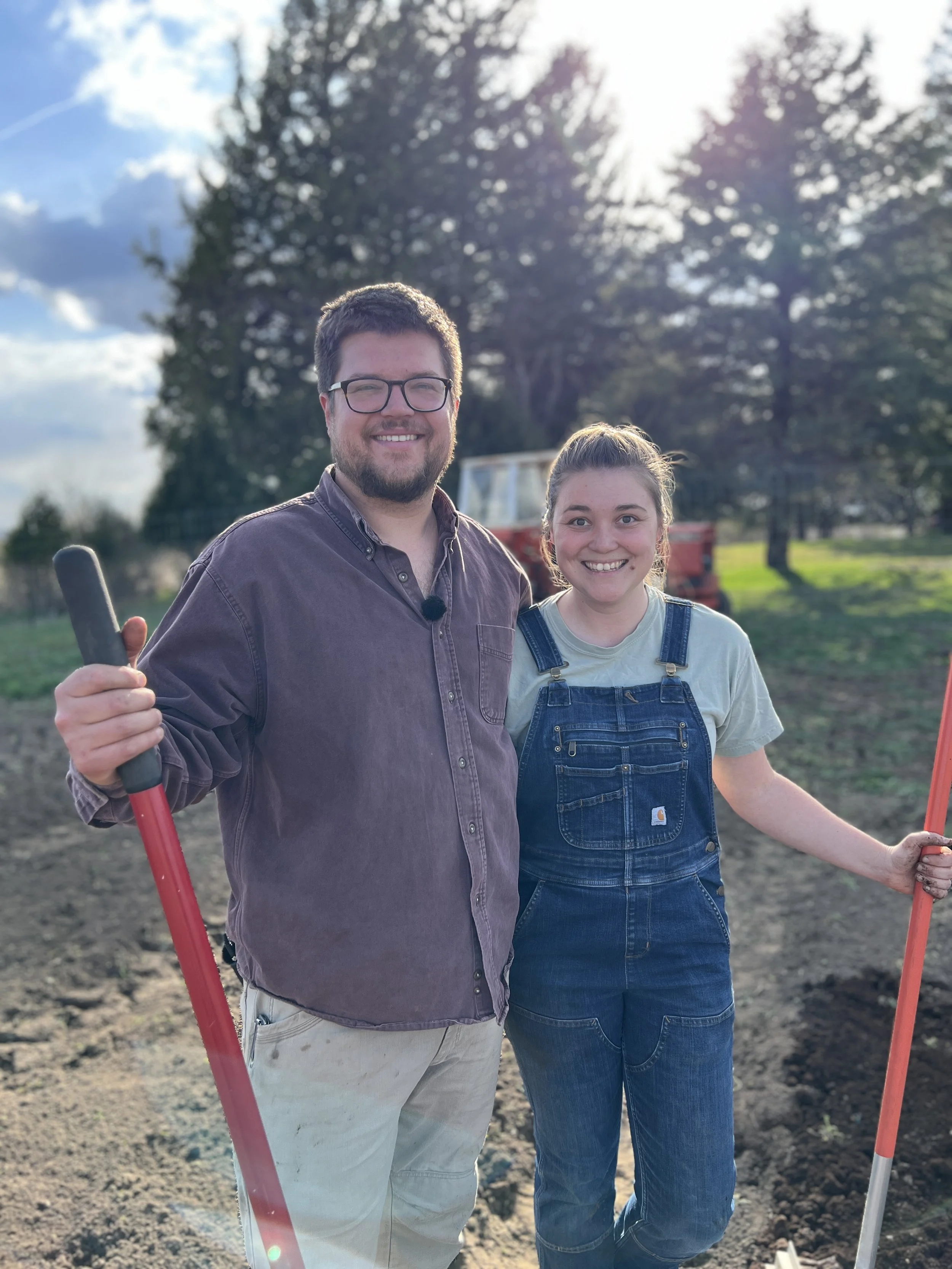 Ethan and Carly an their organic vegetable field on a sunny day holding gardening tools.