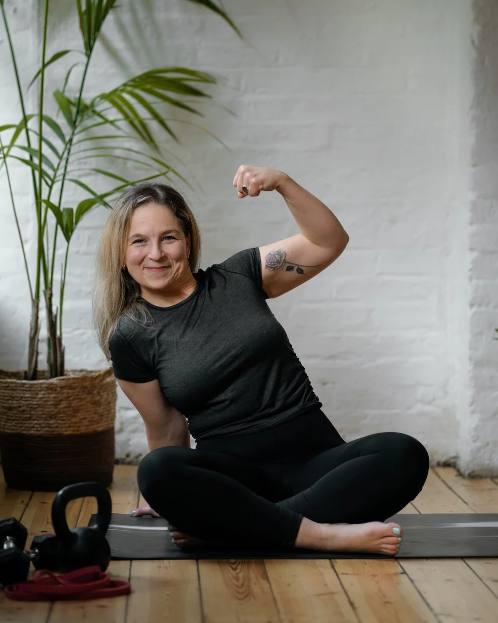 Karima smiling and flexing her arm on a yoga mat