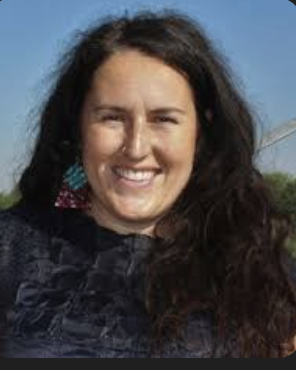 A woman with long dark hair smiling outdoors against a blue sky.