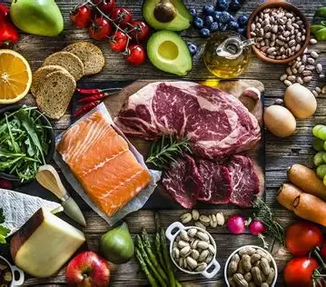 Assorted fresh foods including raw meats, vegetables, fruits, eggs, and nuts on a rustic wooden table.