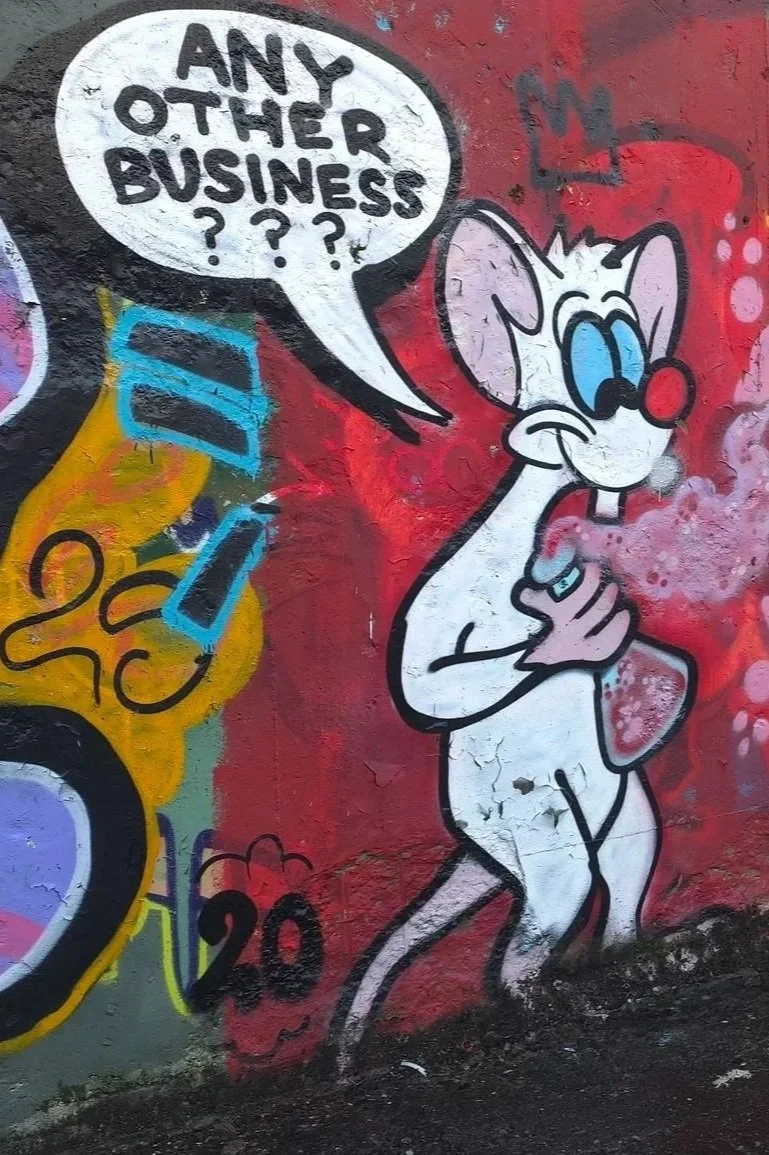 Graffiti art of a cartoon mouse with large blue eyes and a red nose, holding a phone to its mouth, with a speech bubble asking "Any other business???" written inside.