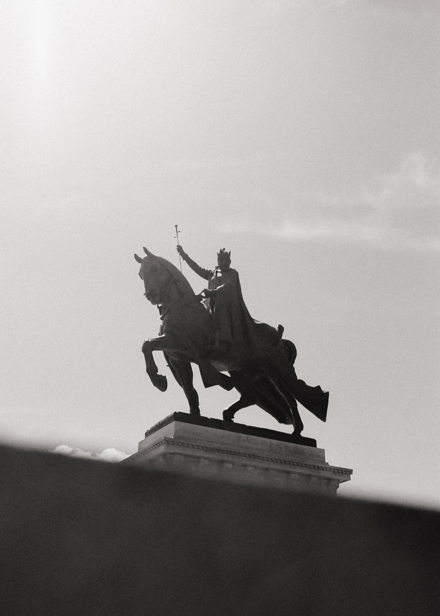A black and white photograph of a statue of a man on a horse, holding a staff in his right hand, atop a pedestal against the sky.