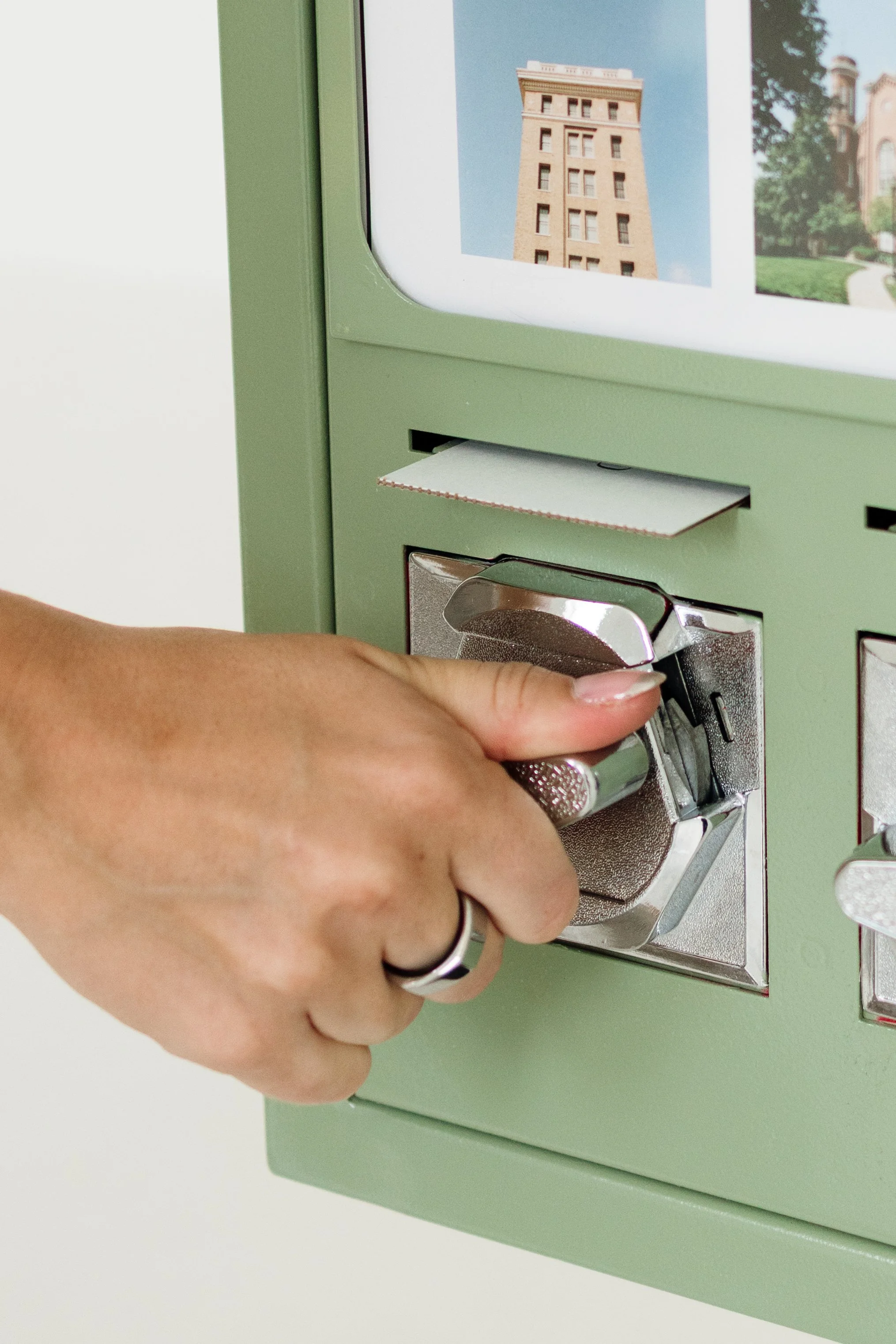 A person with manicured nails is inserting a coin into a green mail deposit box.