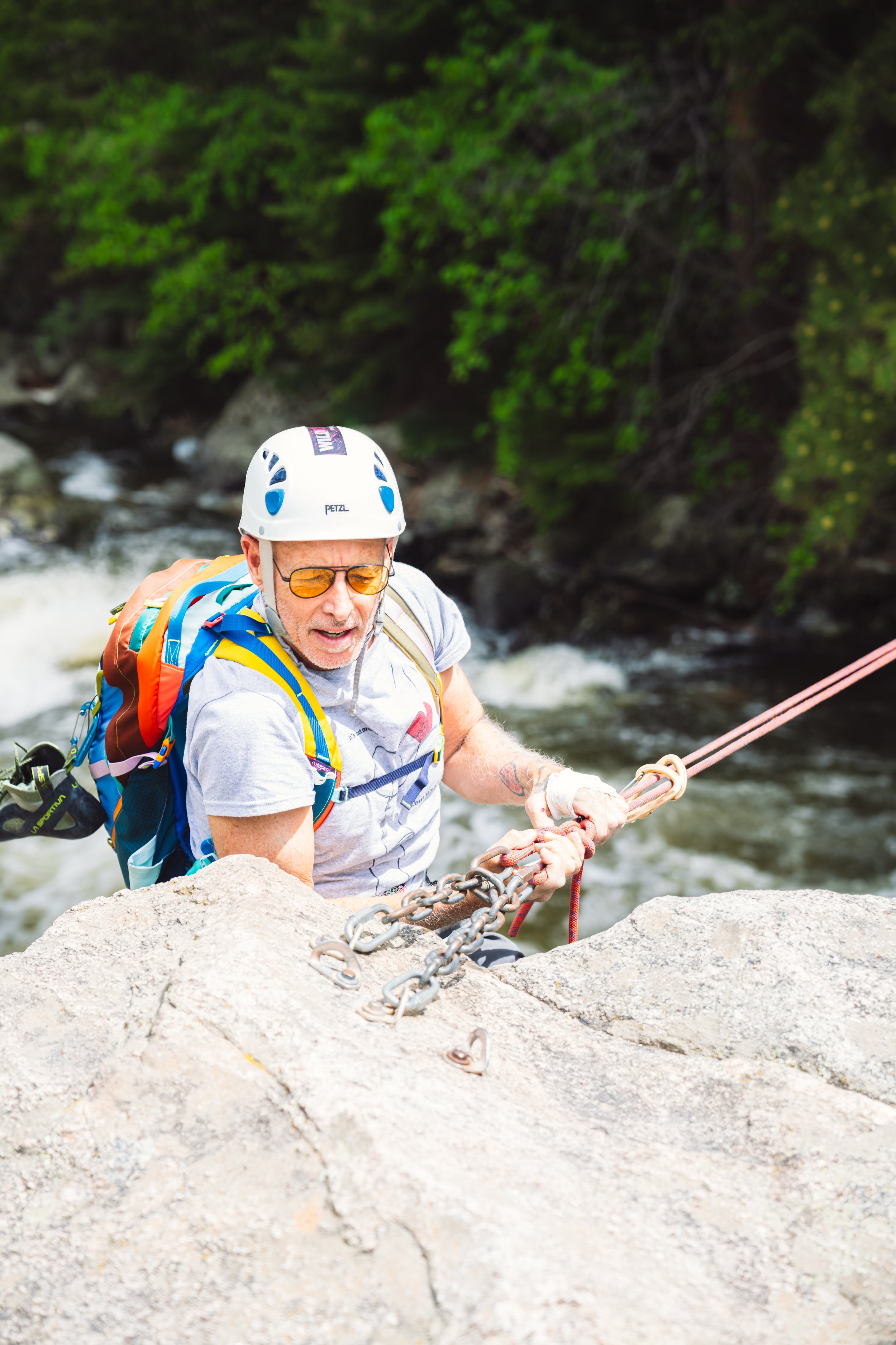 An older man with sunglasses and helmet dismounting from a Tyrolean traverse after crossing Boulder Creek, CO. 
