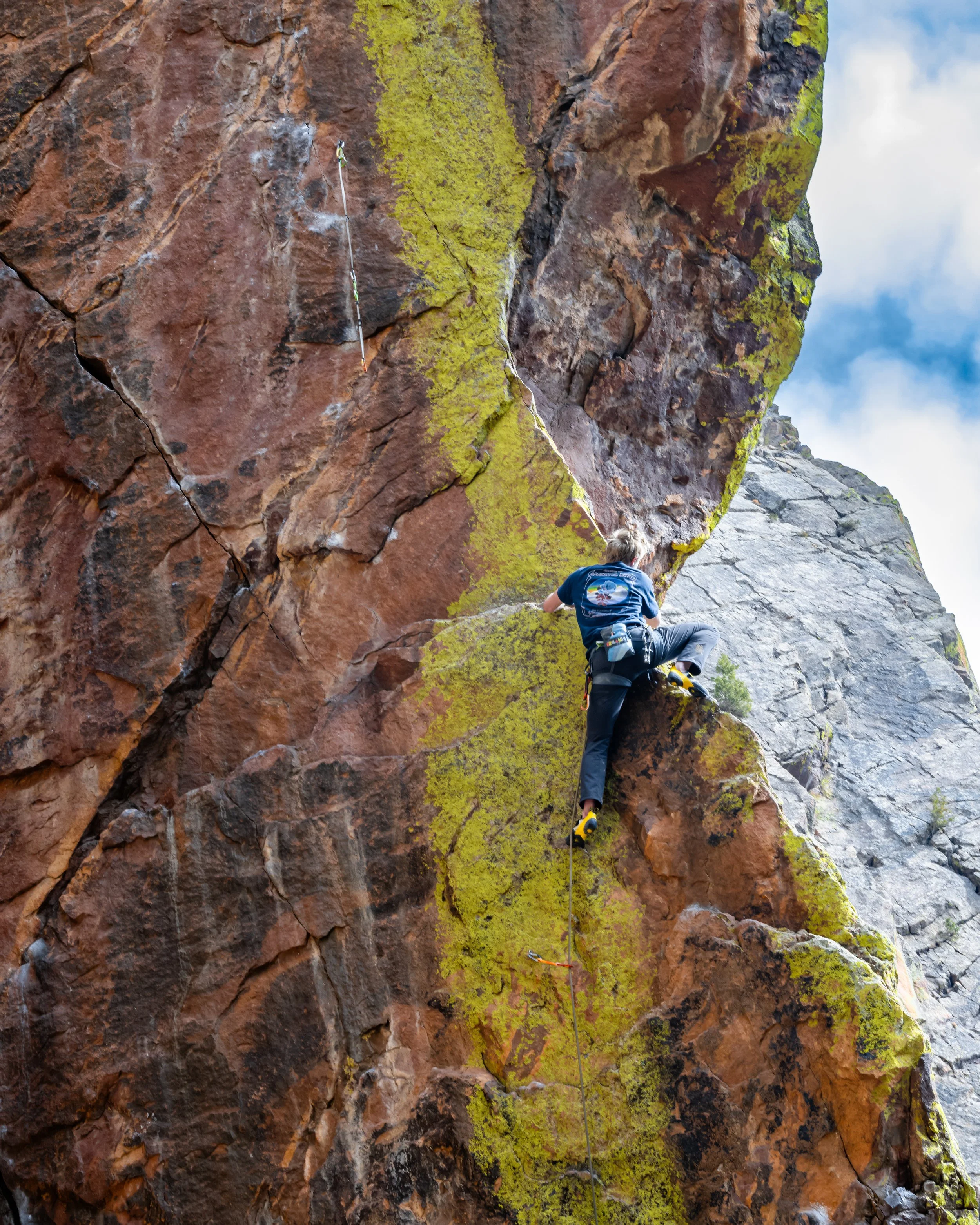 A person rock climbing on the 5.12d route Sayat-Nova, in Eldorado Canyon State Park, CO, wearing a harness and using climbing equipment.