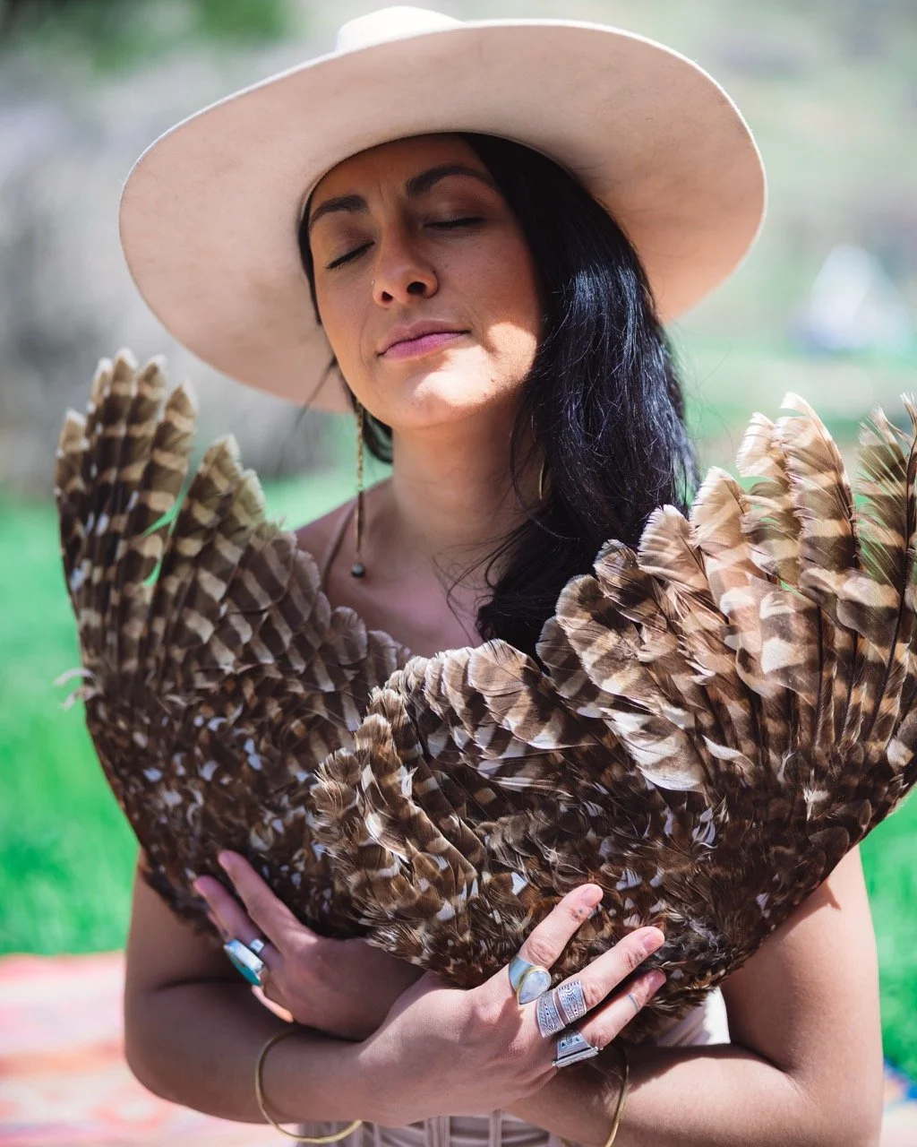 Woman with long dark hair wearing a wide-brimmed hat holding a large arrangement of feathers.