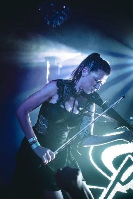 Jessica Borth, playing a keyboard and singing into a microphone, with stage lights in the background.