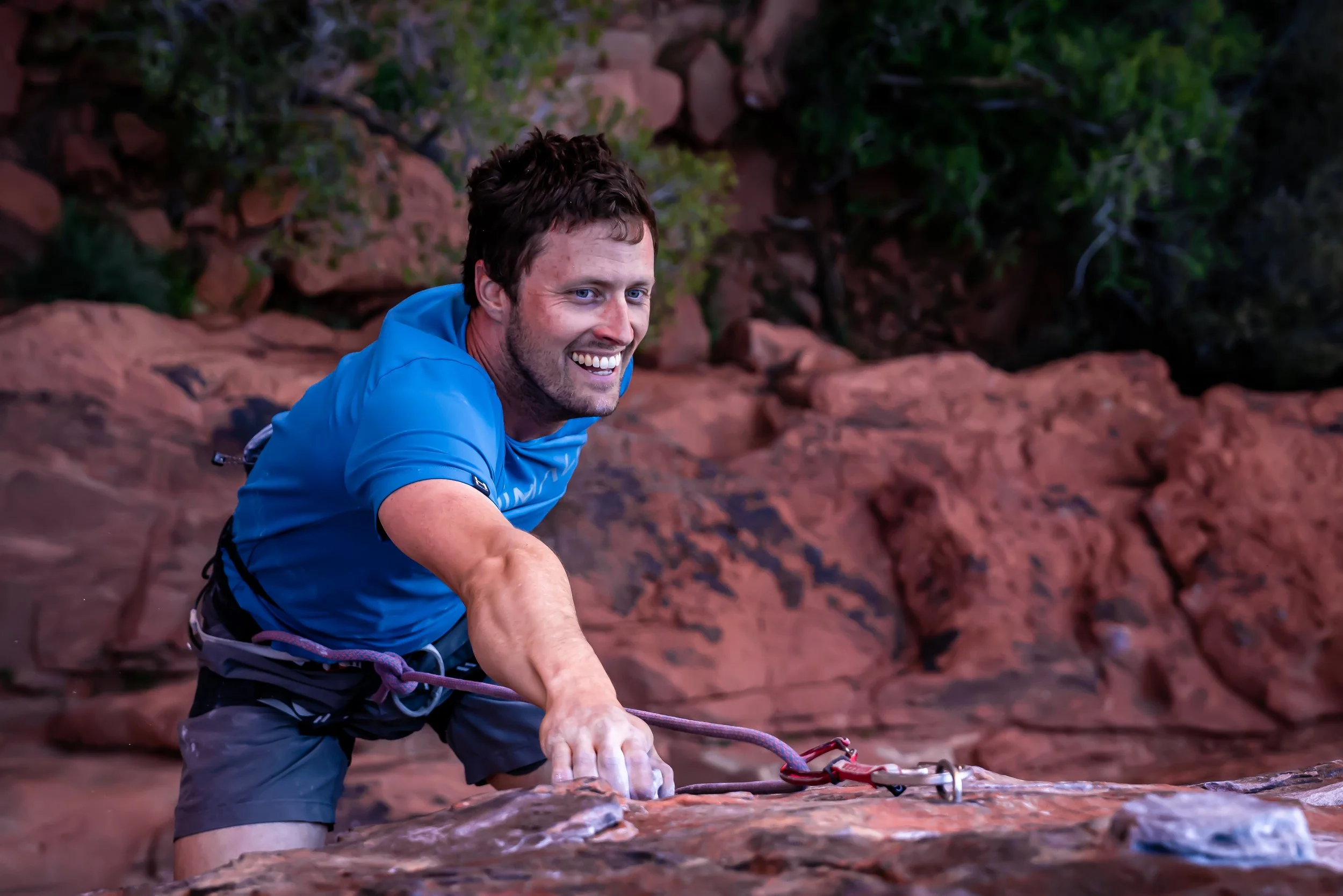 Kevin Capps rock climbing and smiling while gripping a rock with his hand, in Red Rocks Canyon, NV. 