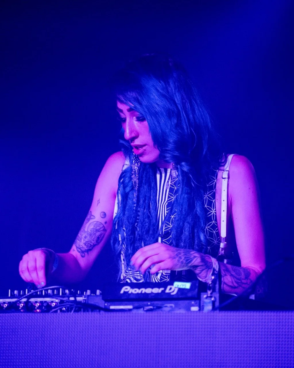 Tesla Nicole performs a set at Cervantes' Other Side, with long dark hair, wearing sleeveless top and working on a Pioneer DJ set. 