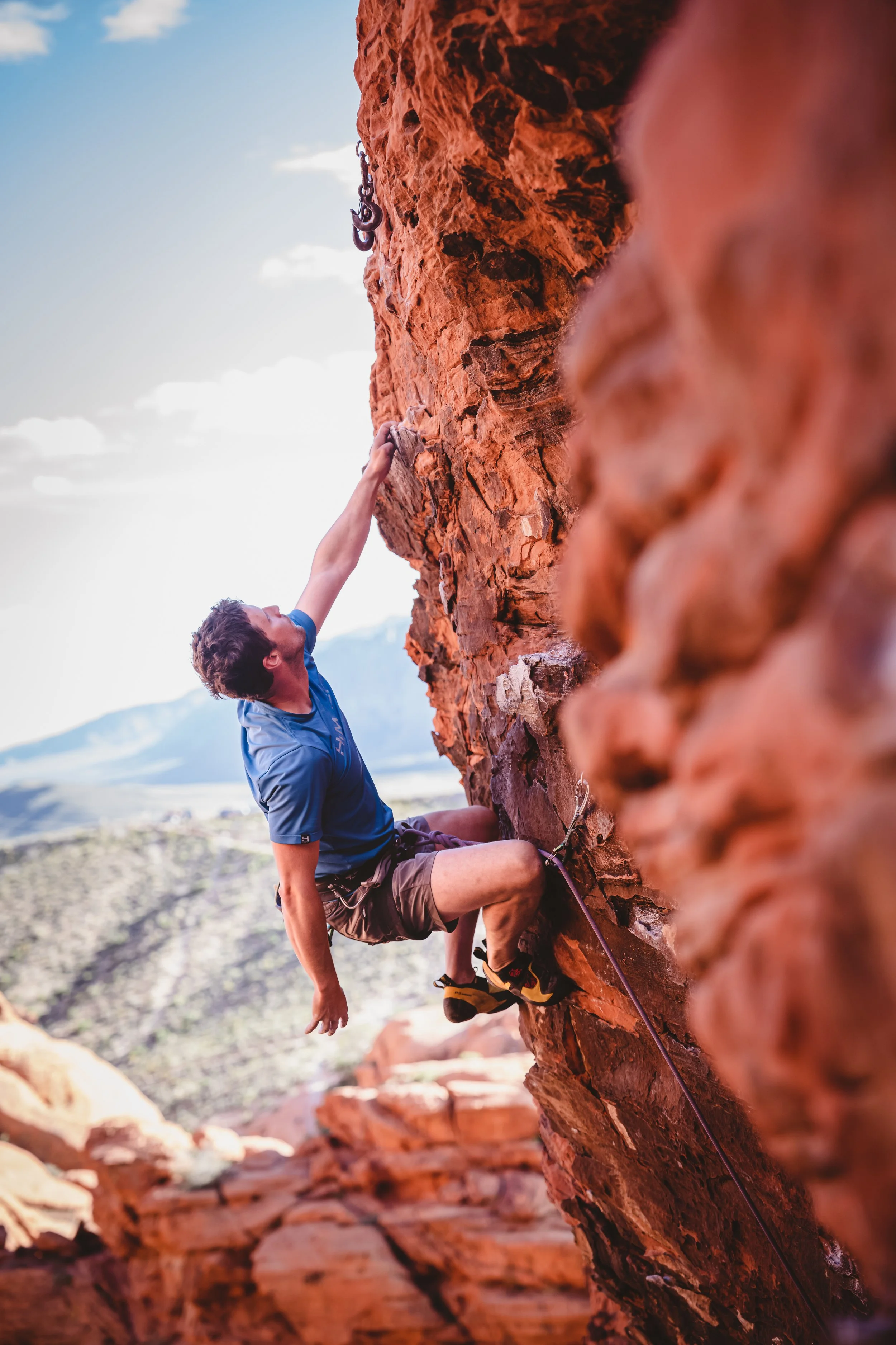 Kevin Capps climbing a red rock cliff in Las Vegas with a mountainous landscape in the background.